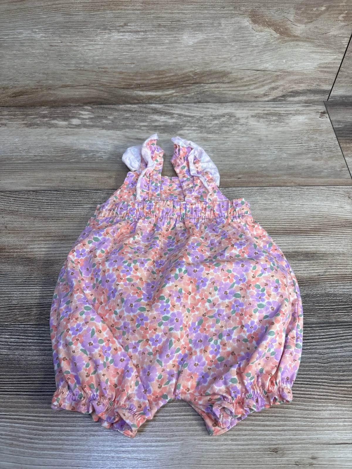 Flat lay of pink floral shortie romper with ruffle straps and elasticized waist and leg openings on wood background