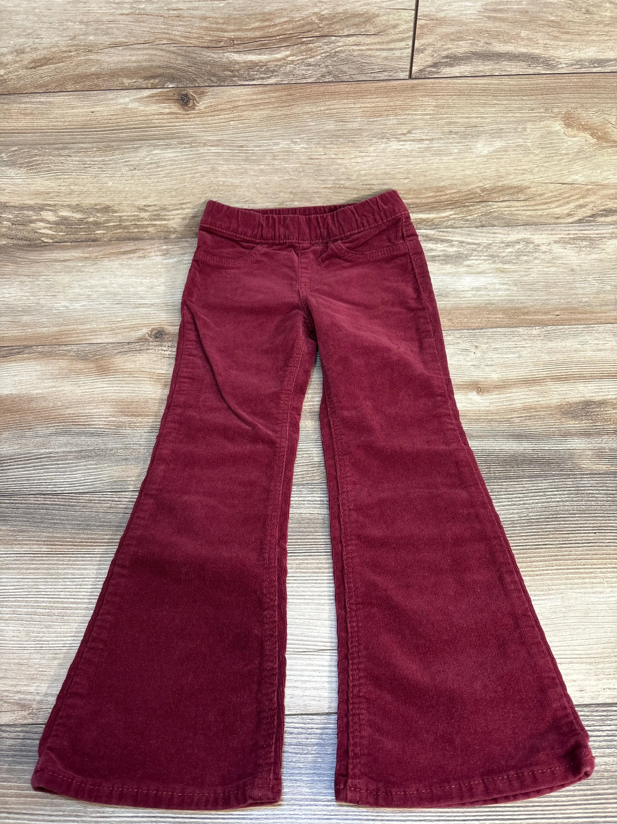 Red corduroy kids bell bottom pants with elastic waistband on wood background