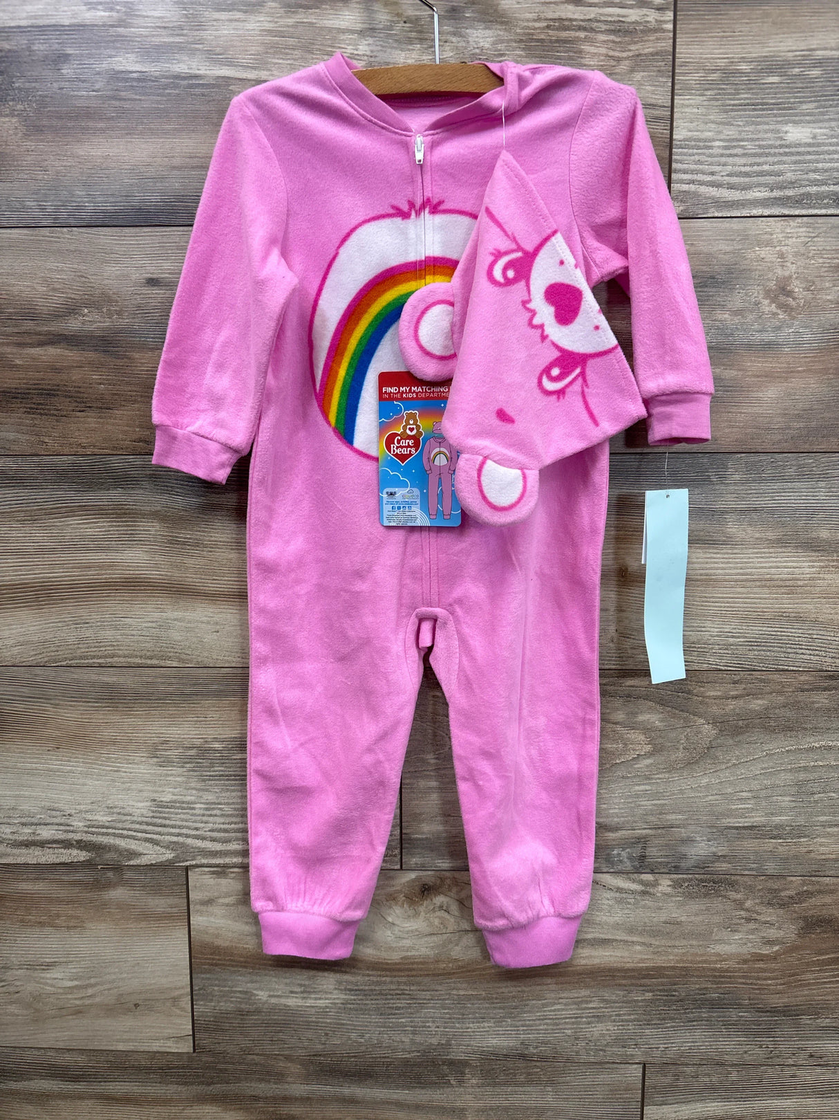 Pink Care Bears baby sleeper with rainbow design and matching hat on wooden background