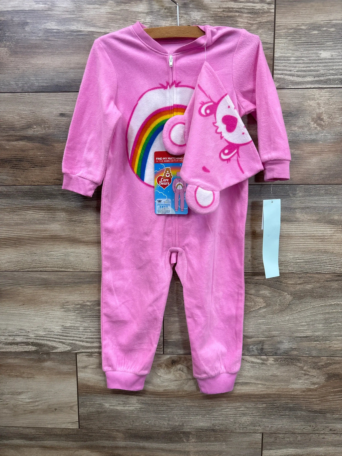 Pink Care Bears baby sleeper with rainbow design and matching hat on wooden background