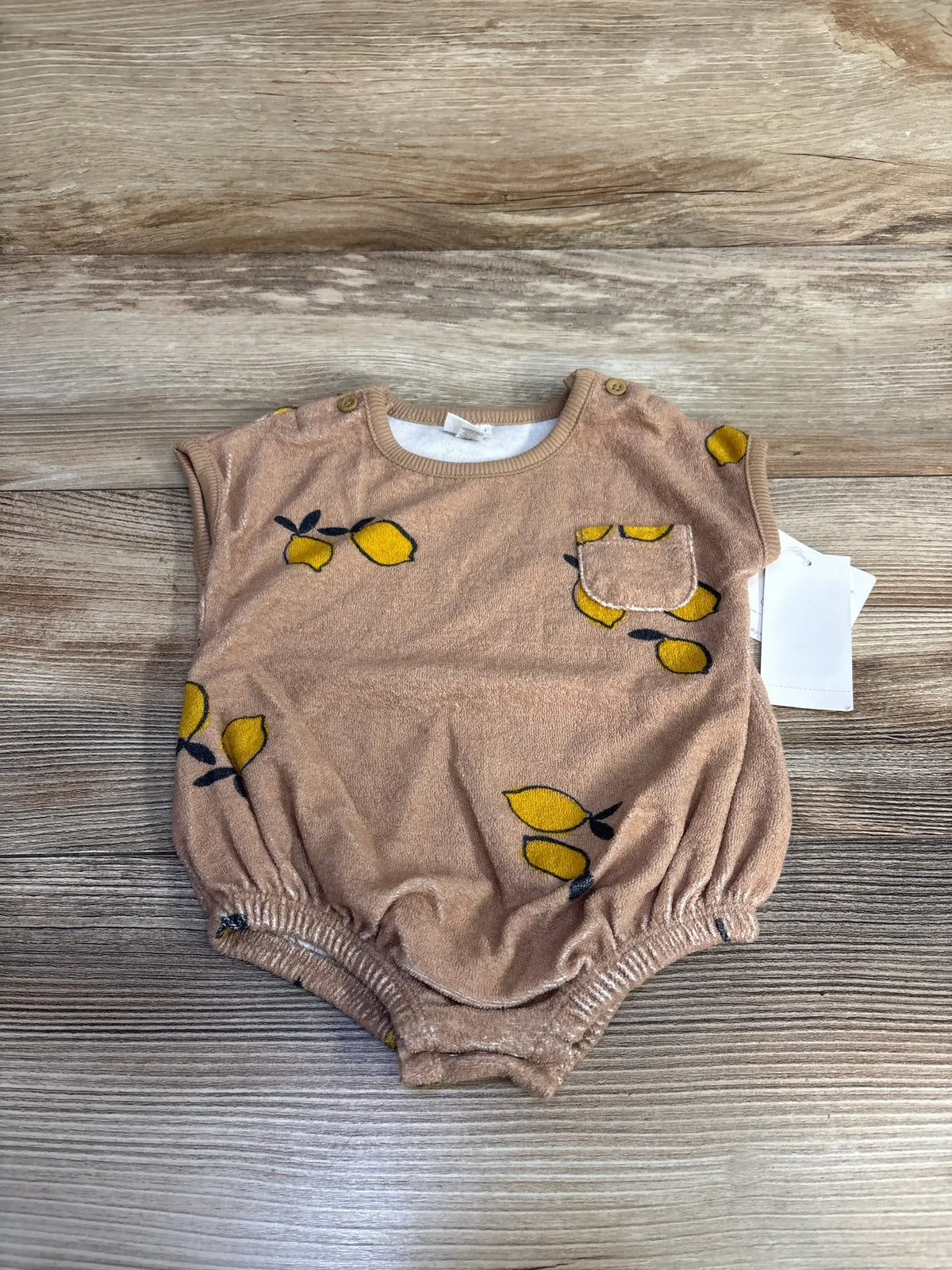 Flat lay of brown terry cloth baby romper 0-3M with yellow lemon print, chest pocket, shoulder snaps, elastic leg openings on wood