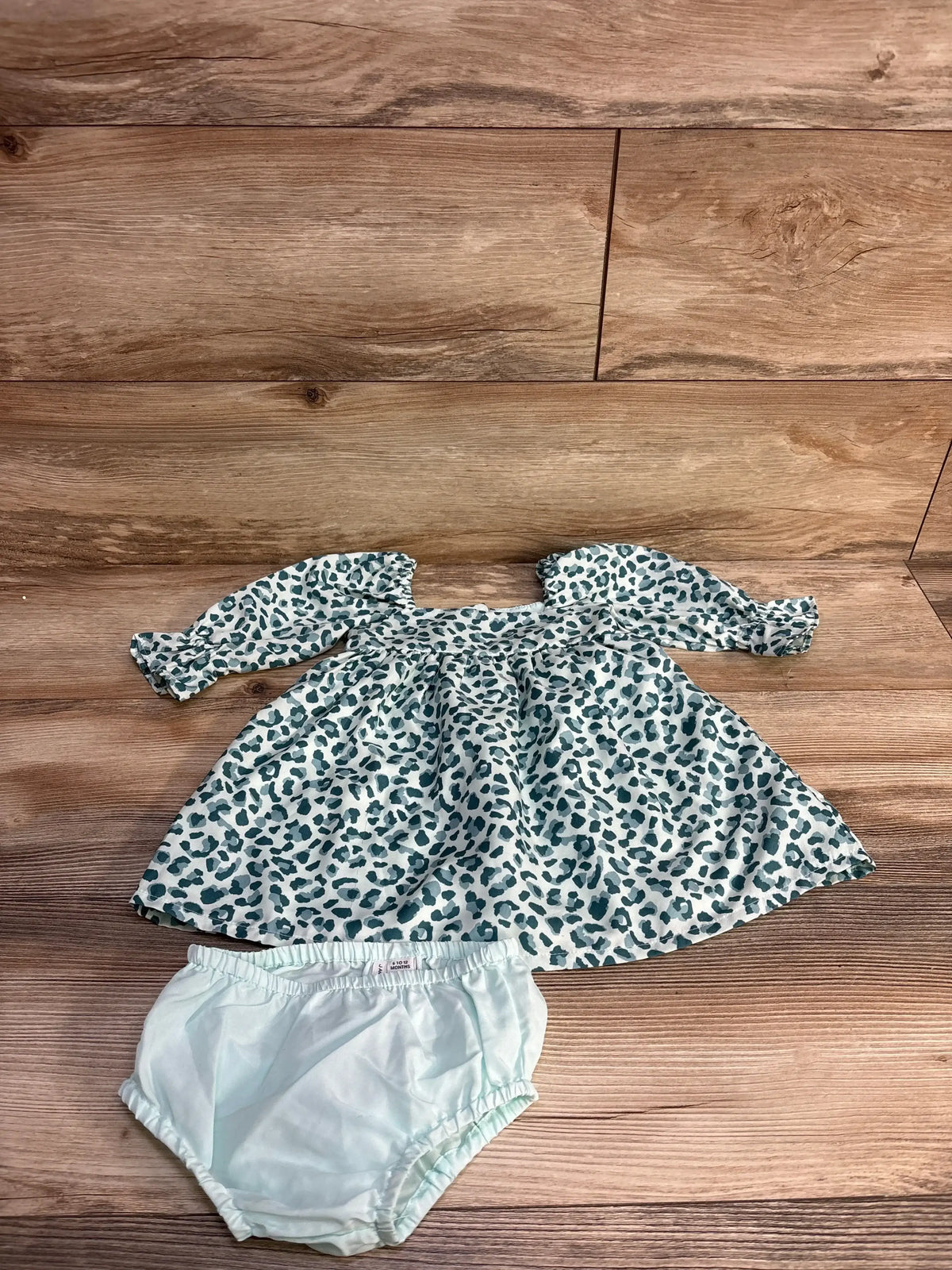 Flat lay of Janie and Jack two-piece leopard twill dress with puff sleeves and matching light blue bloomers on wood background