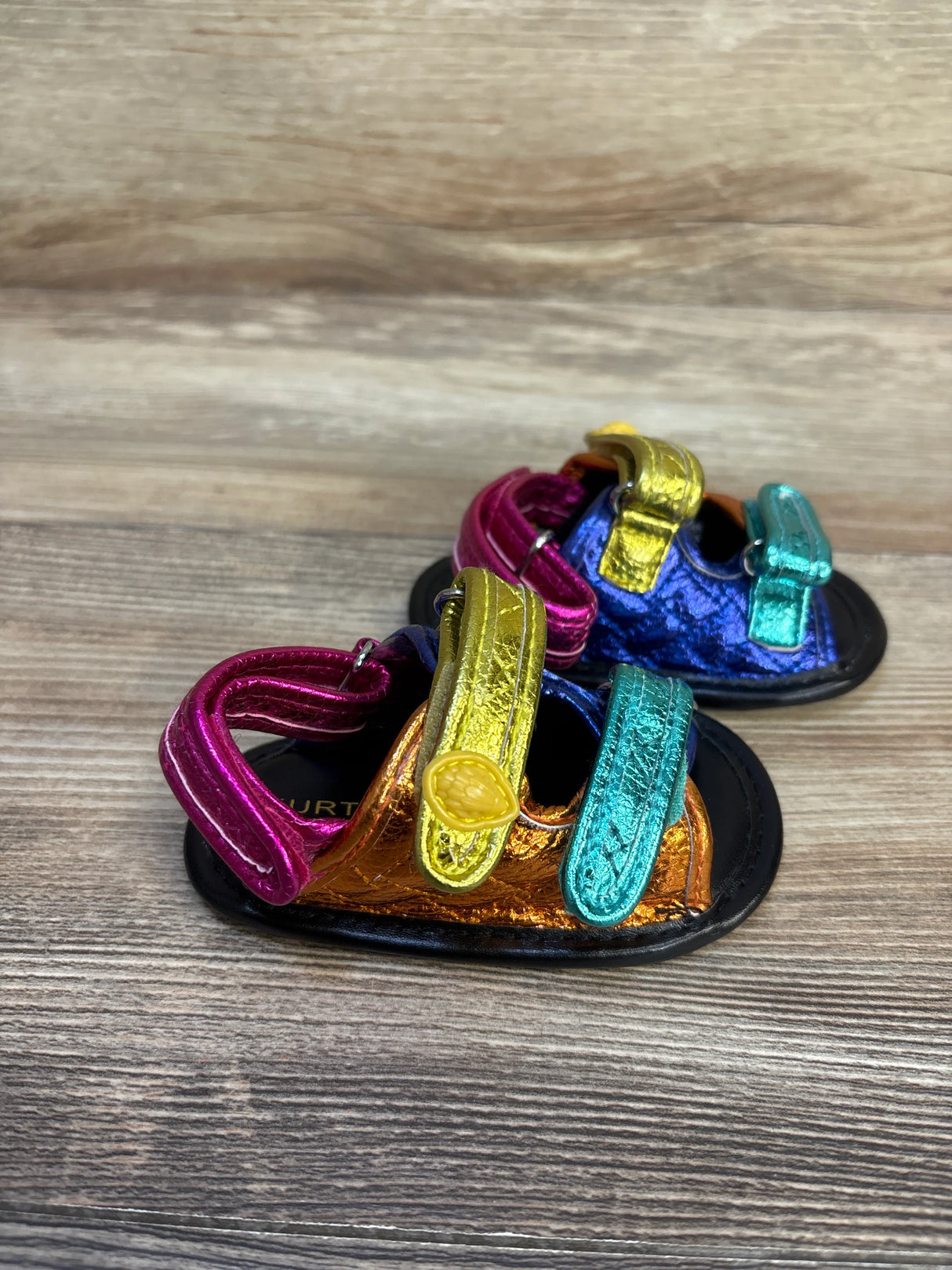 Colorful metallic baby sandals with velcro straps on wood background