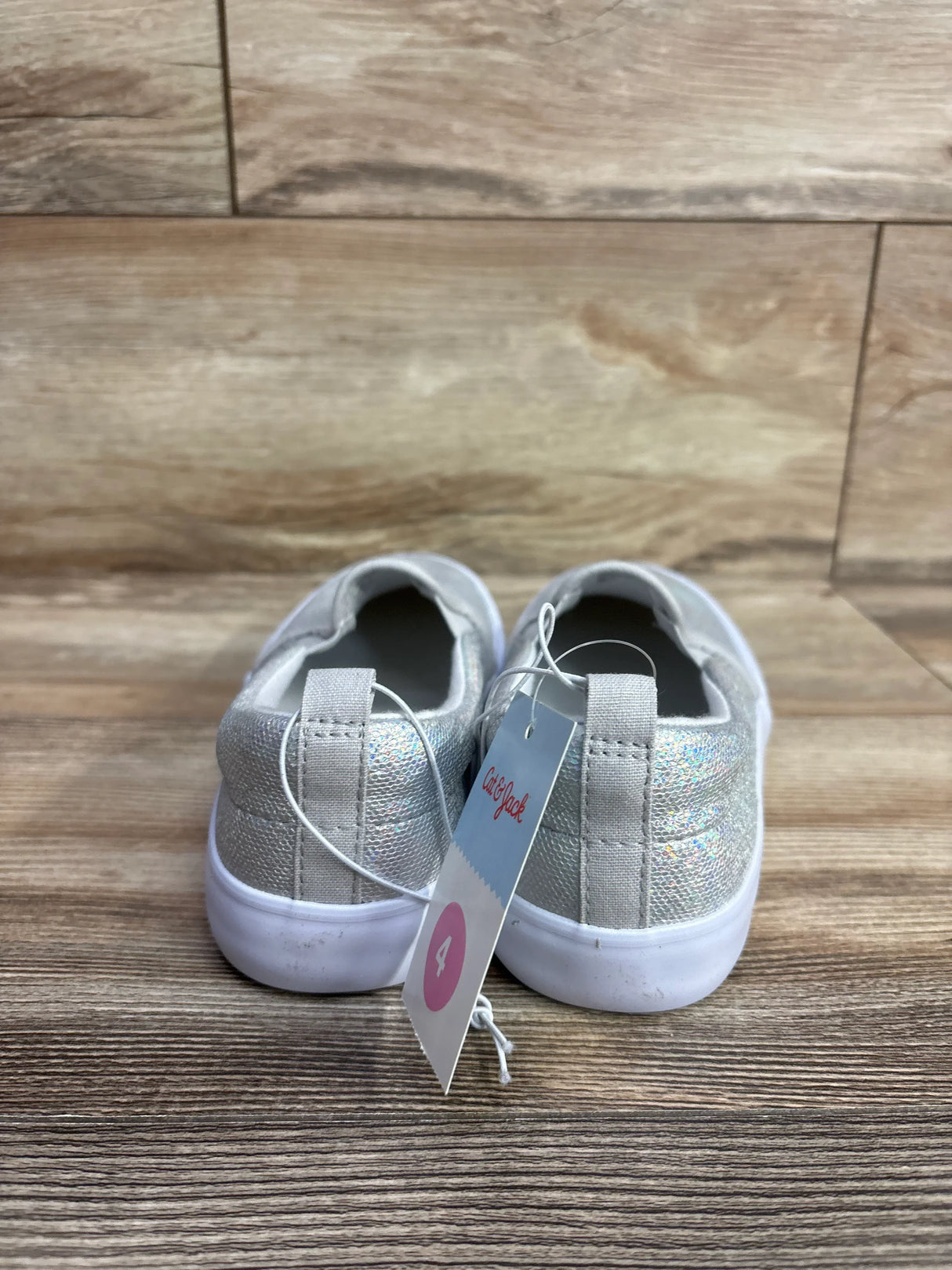 Pair of kids' silver glitter slip-on shoes with white soles, size 4, on wooden floor