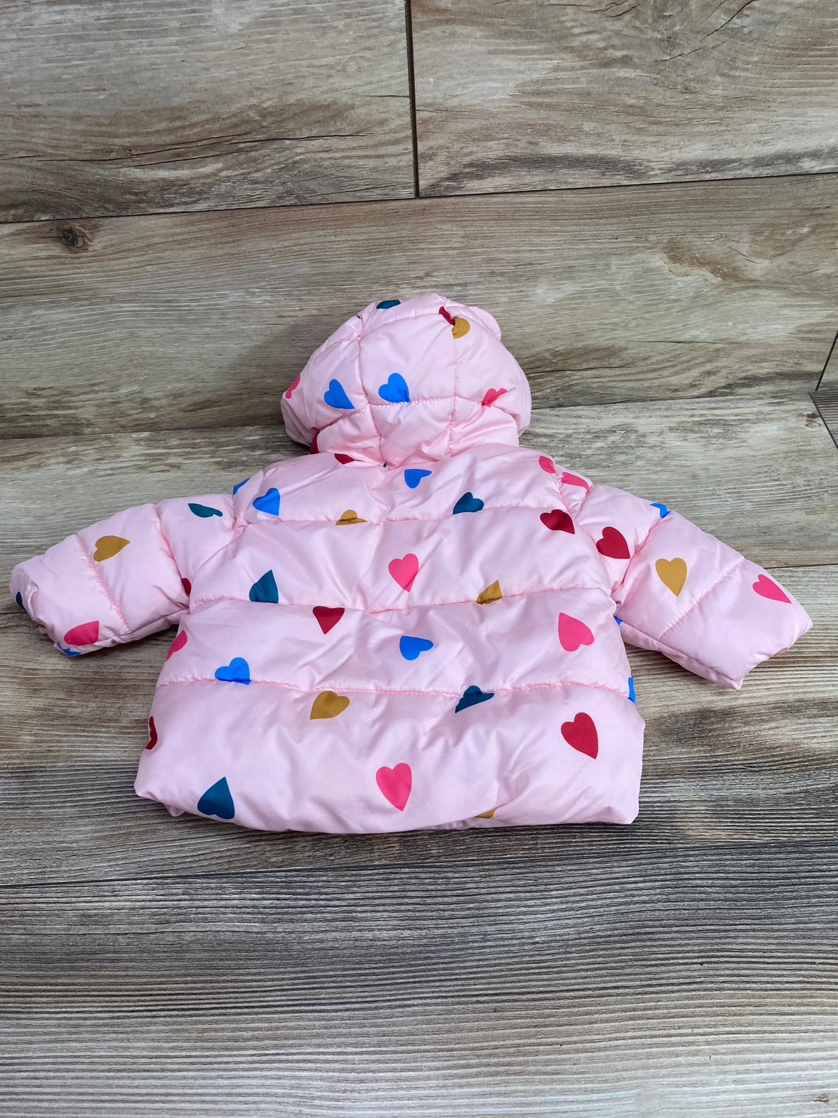 Back view of pink hooded puffer jacket showcasing a colorful heart pattern and quilted design on a wood floor