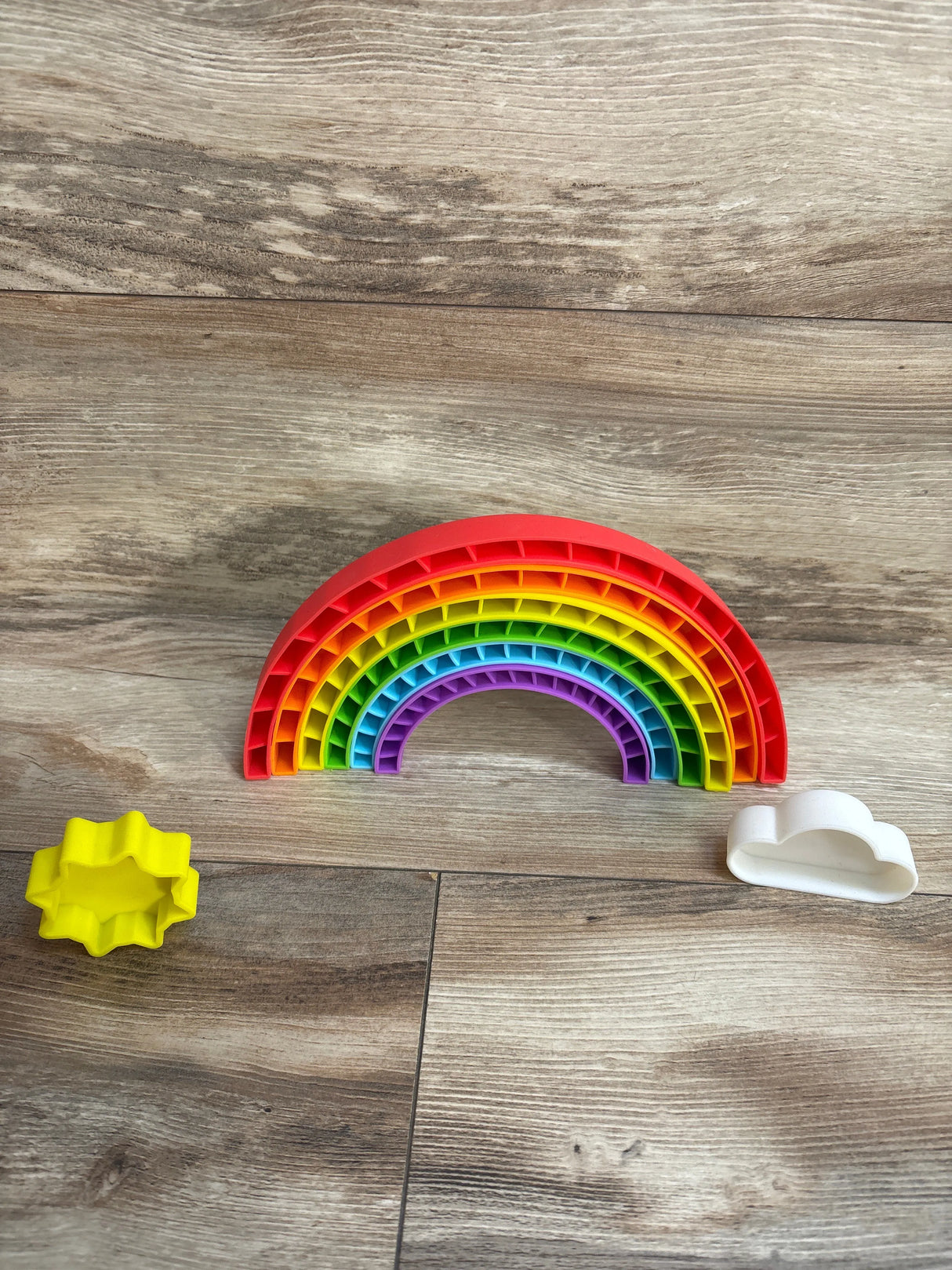 Rainbow stacking toy with yellow star and white cloud cutters on wood floor
