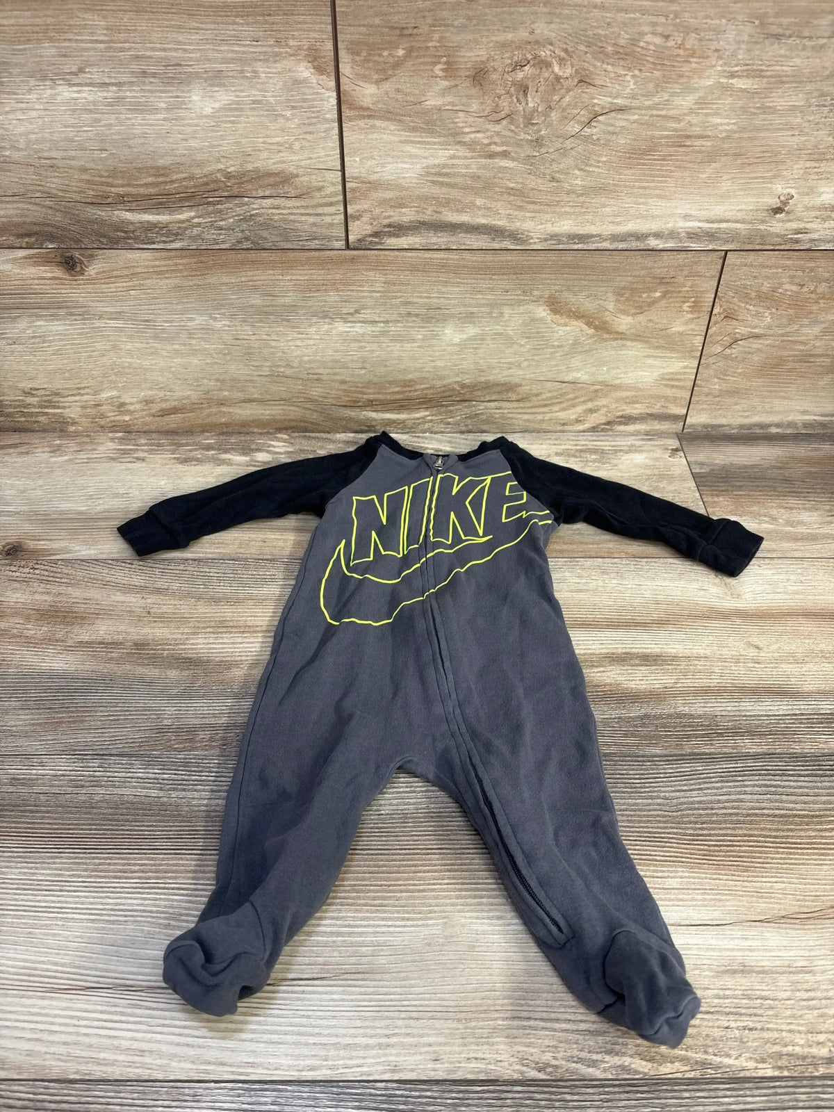 Flat-lay of black/gray Nike baby sleeper 6M with front zipper and neon yellow logo on wood floor