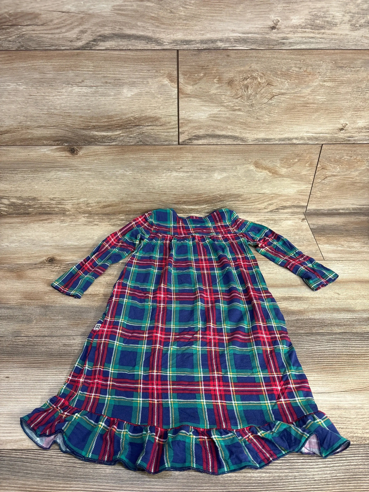 Plaid toddler dress with ruffled hem, festive red green blue pattern, laid on wood floor