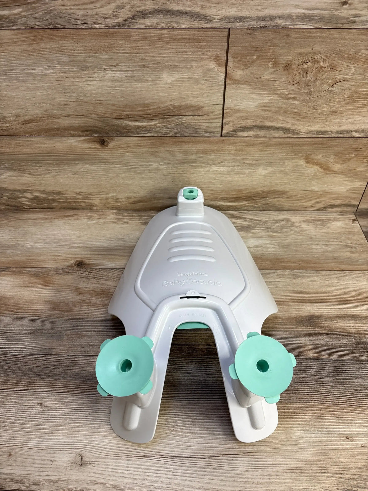 Overhead view of Semplicitas Baby Bath for sink showing white U-shaped bath with two mint-green suction cups on wood surface