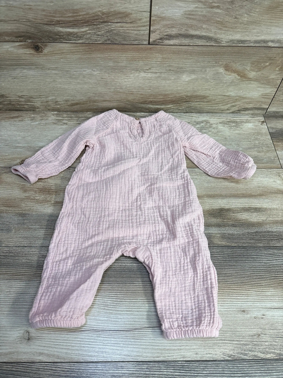 Pink long sleeve baby romper with textured fabric, laid flat on wooden floor