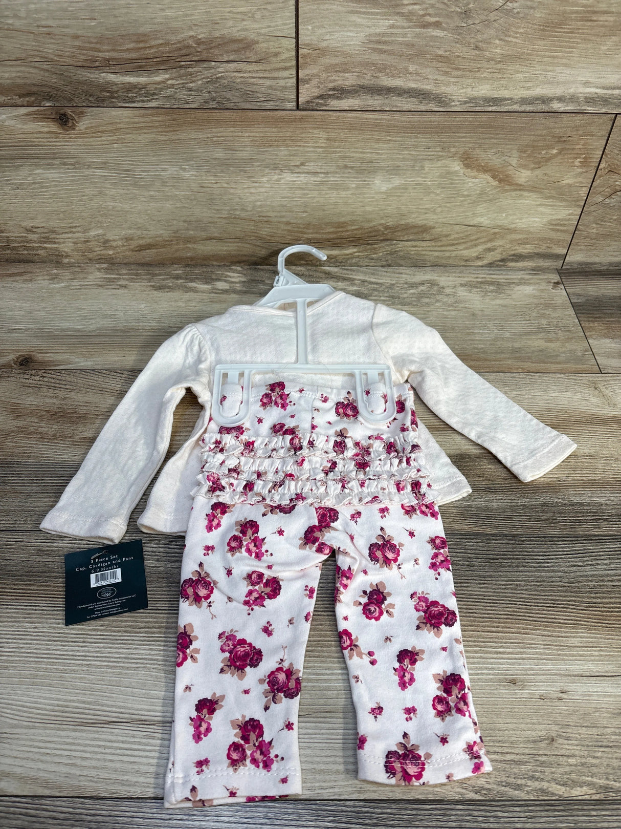 Infant floral ruffle pants and cream long-sleeve top set on a hanger, wood background