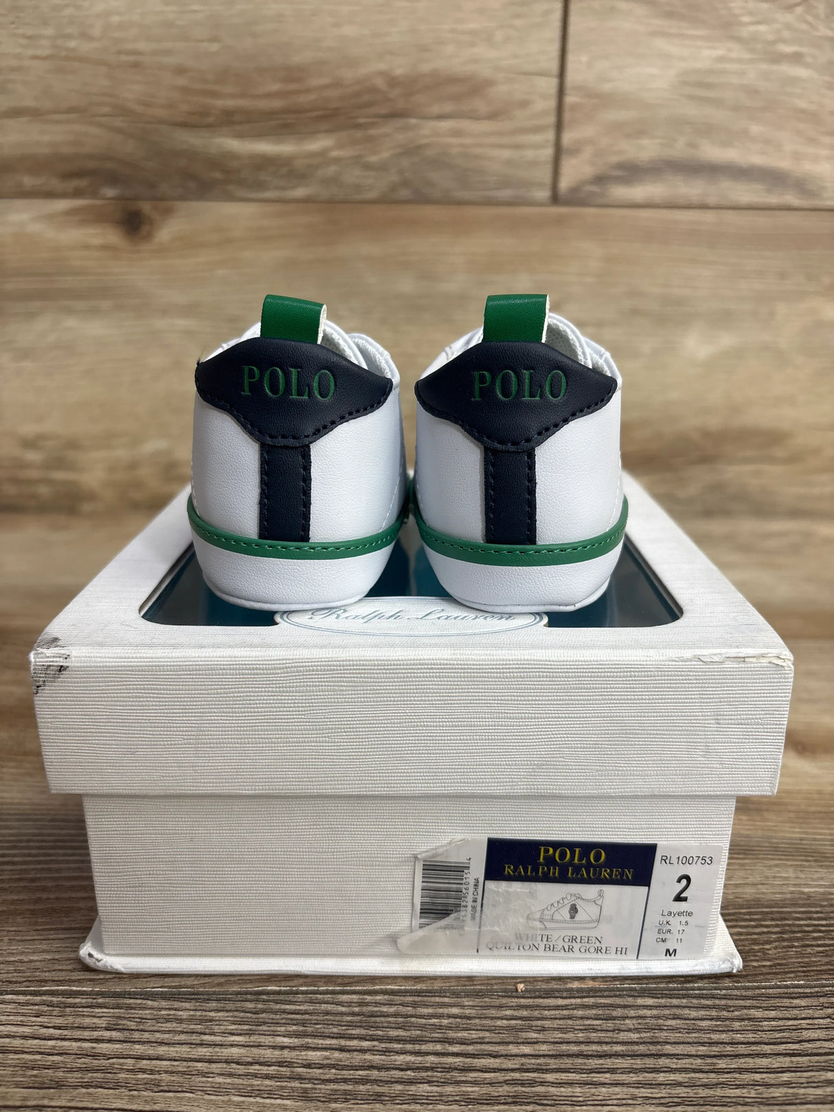 Back view of white and green Polo Ralph Lauren baby shoes on a worn white box