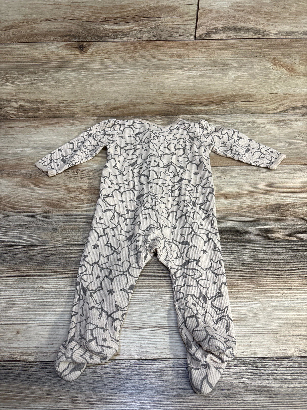 Beige baby footed onesie with gray floral pattern on wood floor