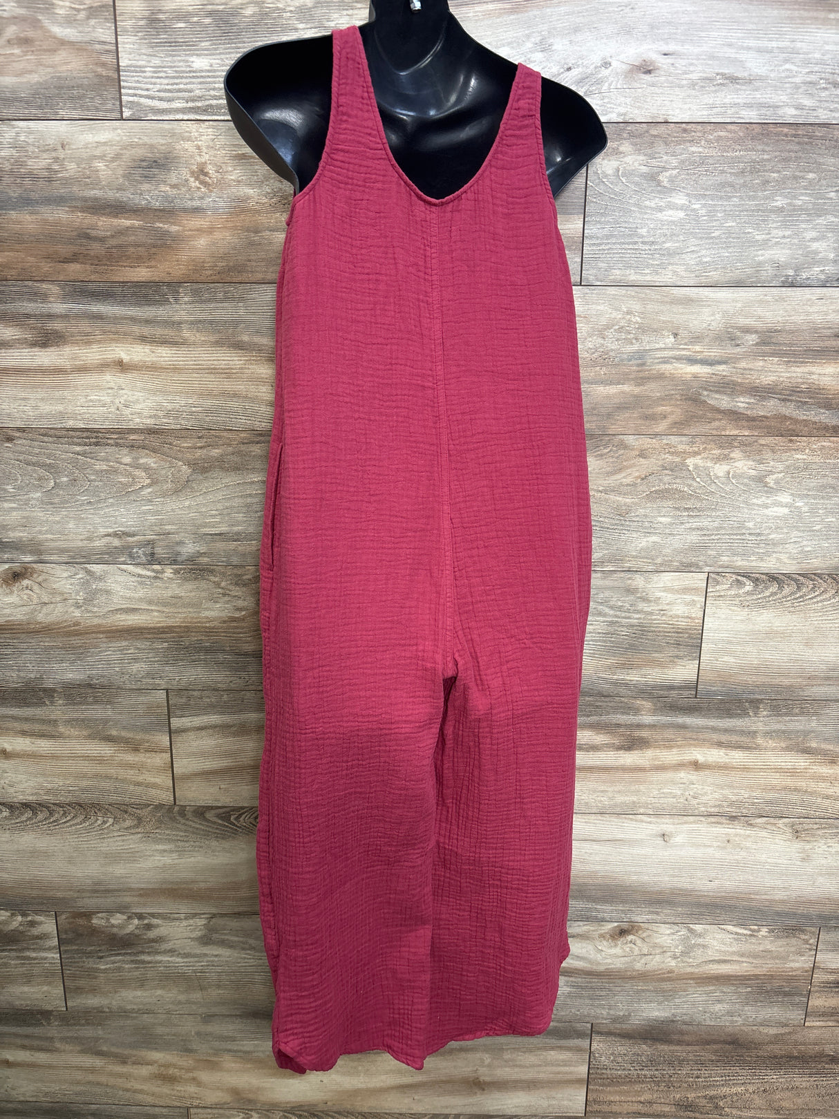 Front view of burgundy maternity gauze jumpsuit with V-neck and wide legs on a black mannequin against wood background