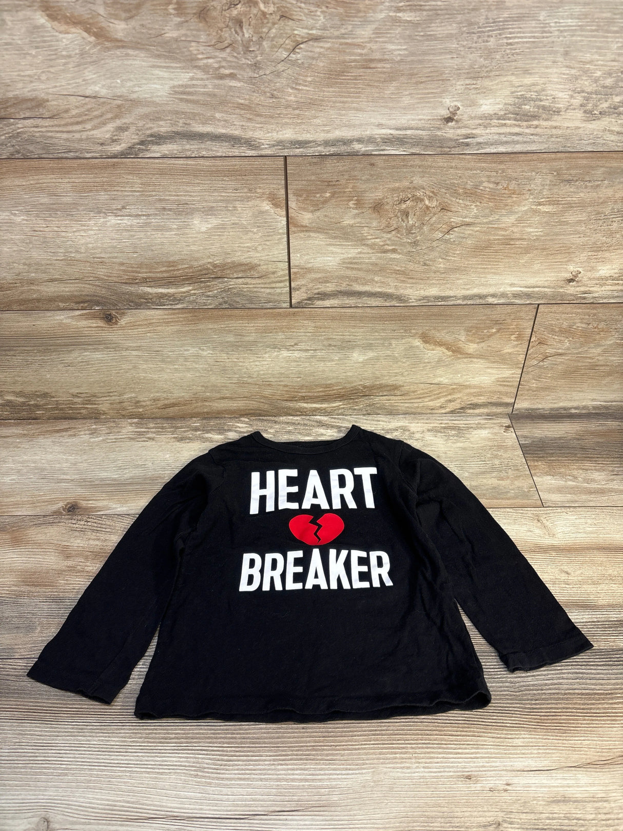 Black long sleeve kids shirt with 'Heart Breaker' and red broken heart graphic on wood floor