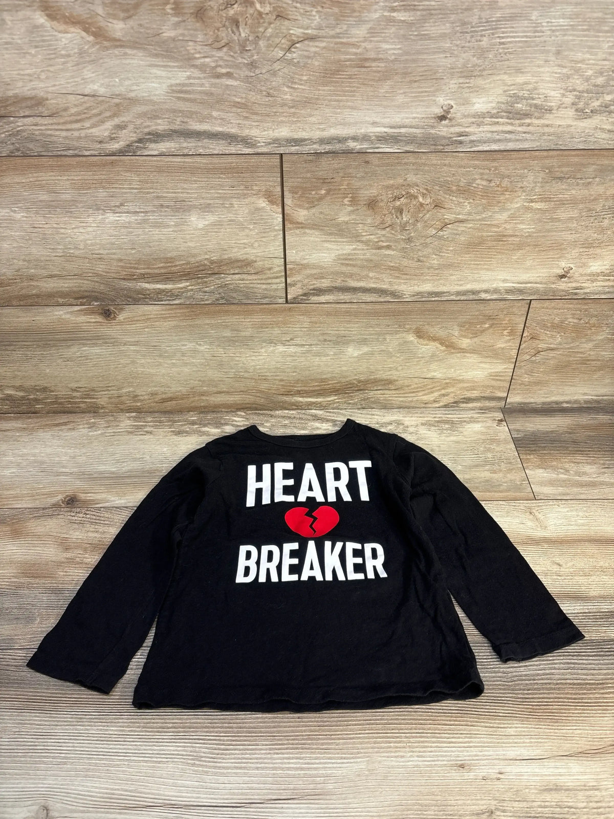 Black long sleeve kids shirt with 'Heart Breaker' and red broken heart graphic on wood floor