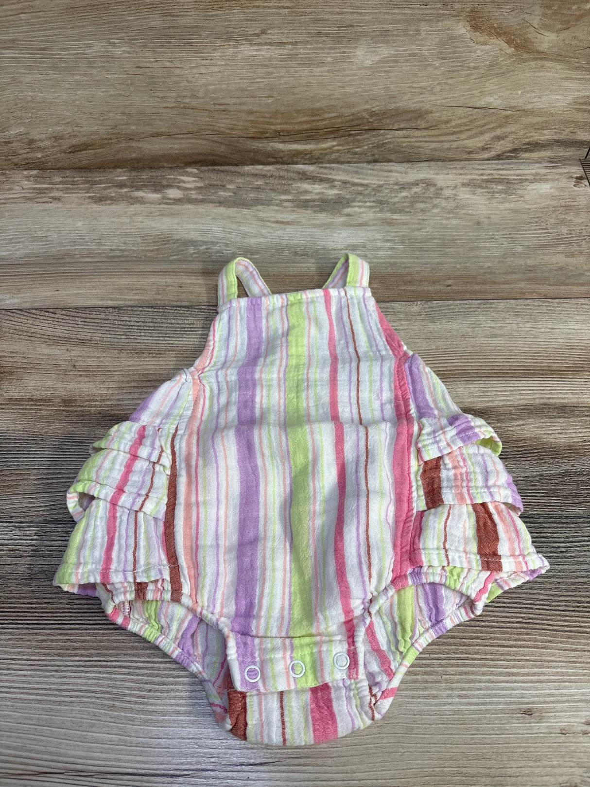 Flat lay of Okie Dokie ruffle baby romper with pastel stripes, ruffled side sleeves and snap crotch on wood background