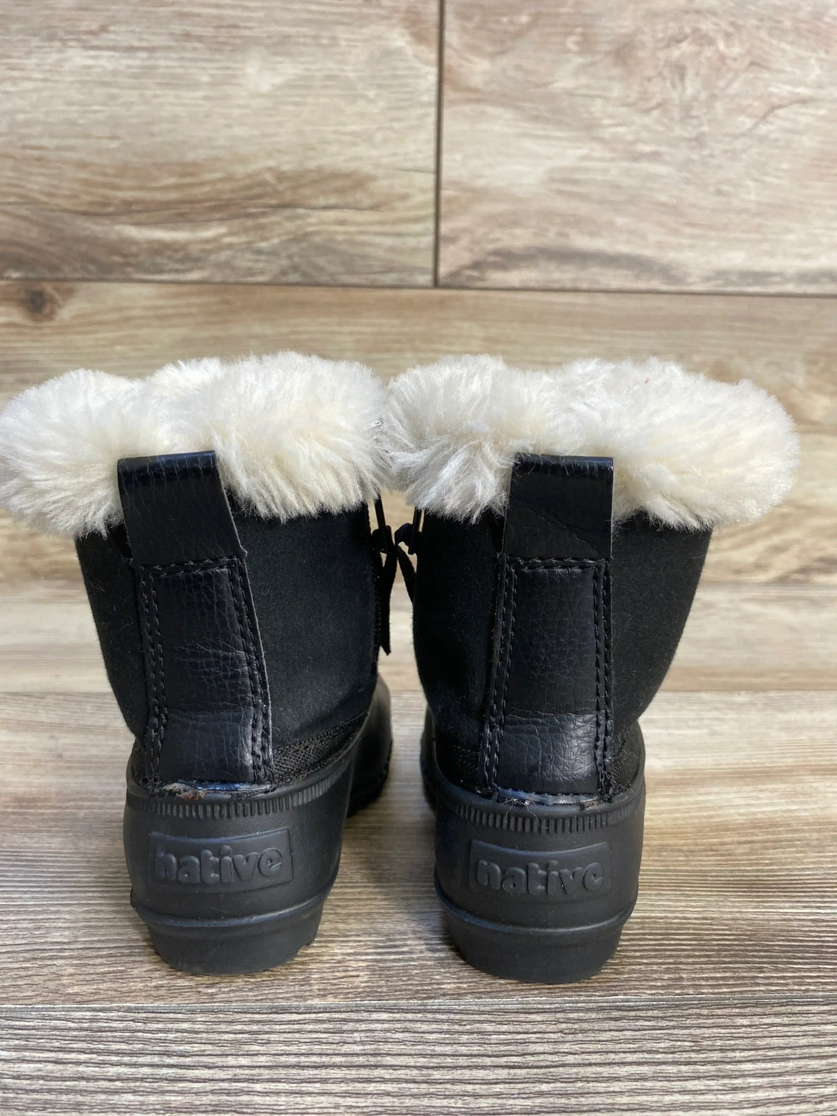 Black kids' winter boots with faux fur lining and Native branding, on wood floor