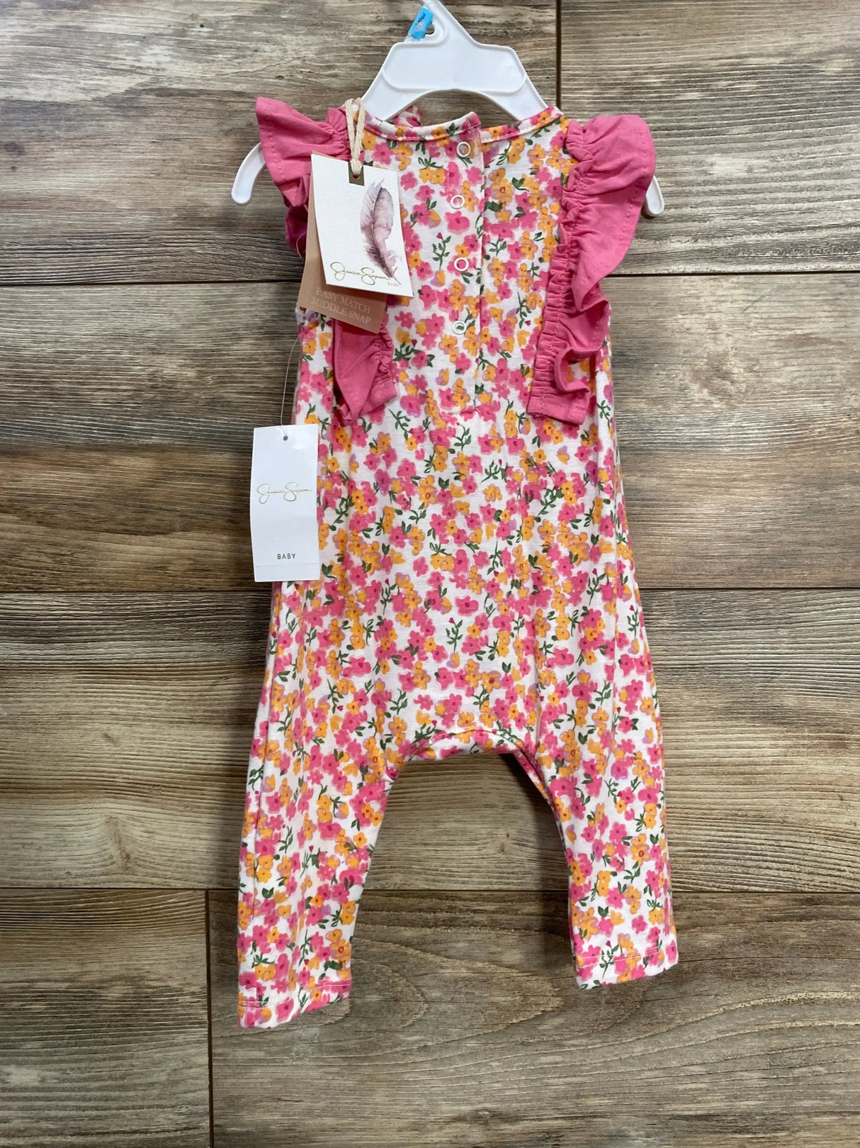 Front view of floral romper with pink ruffle sleeves and headband, size 3-6 months, on hanger over wood background