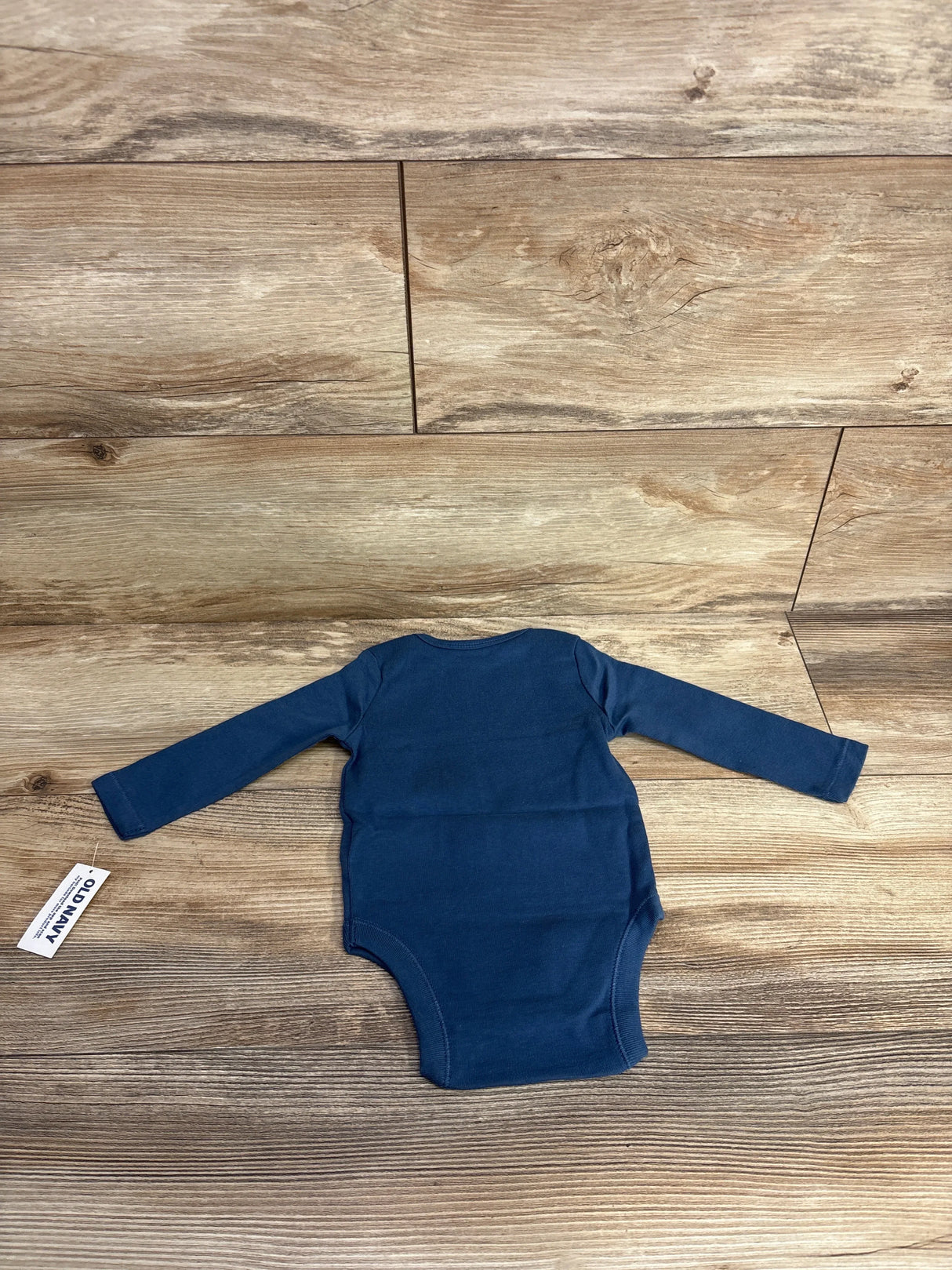 Navy blue long sleeve baby bodysuit with Old Navy tag on wood background