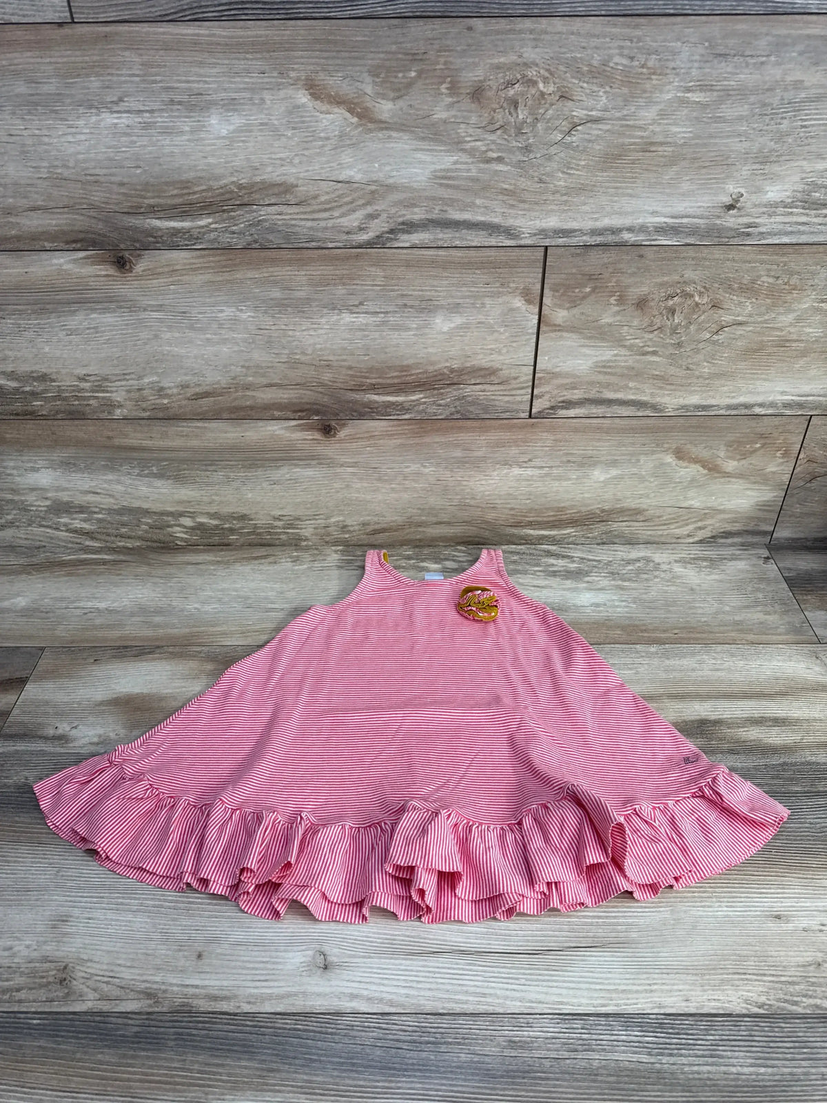 Flat lay of Petit Bateau toddler pink and white striped flare dress showing ruffled hem and yellow flower applique on wood background