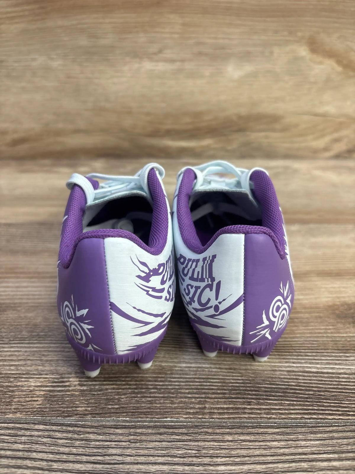 Rear view of Puma x Christian Pulisic Tacto II soccer cleats in Dewdrop Ultraviolet showing graphic heel panels on wood grain