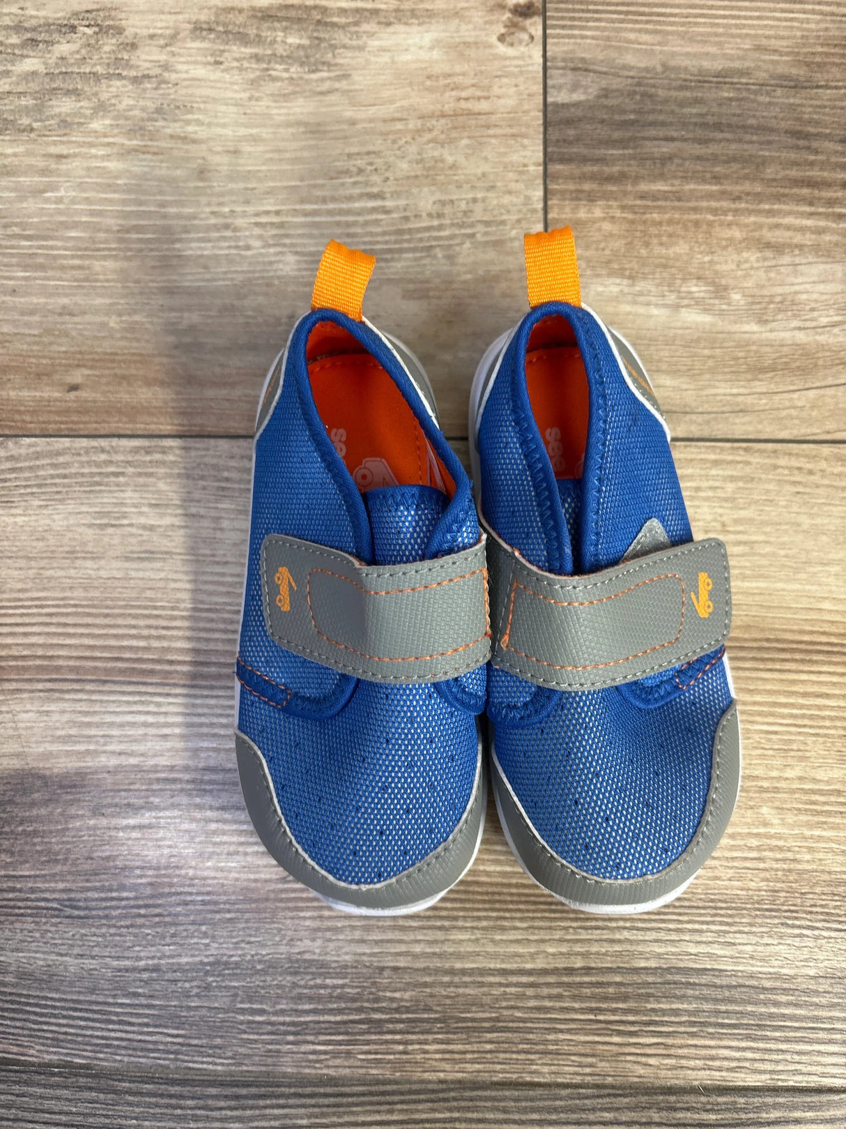 Top-down view of See Kai Run Ryder FlexiRun water shoes showing blue mesh upper, gray Velcro strap, orange heel pull tab on wood floor