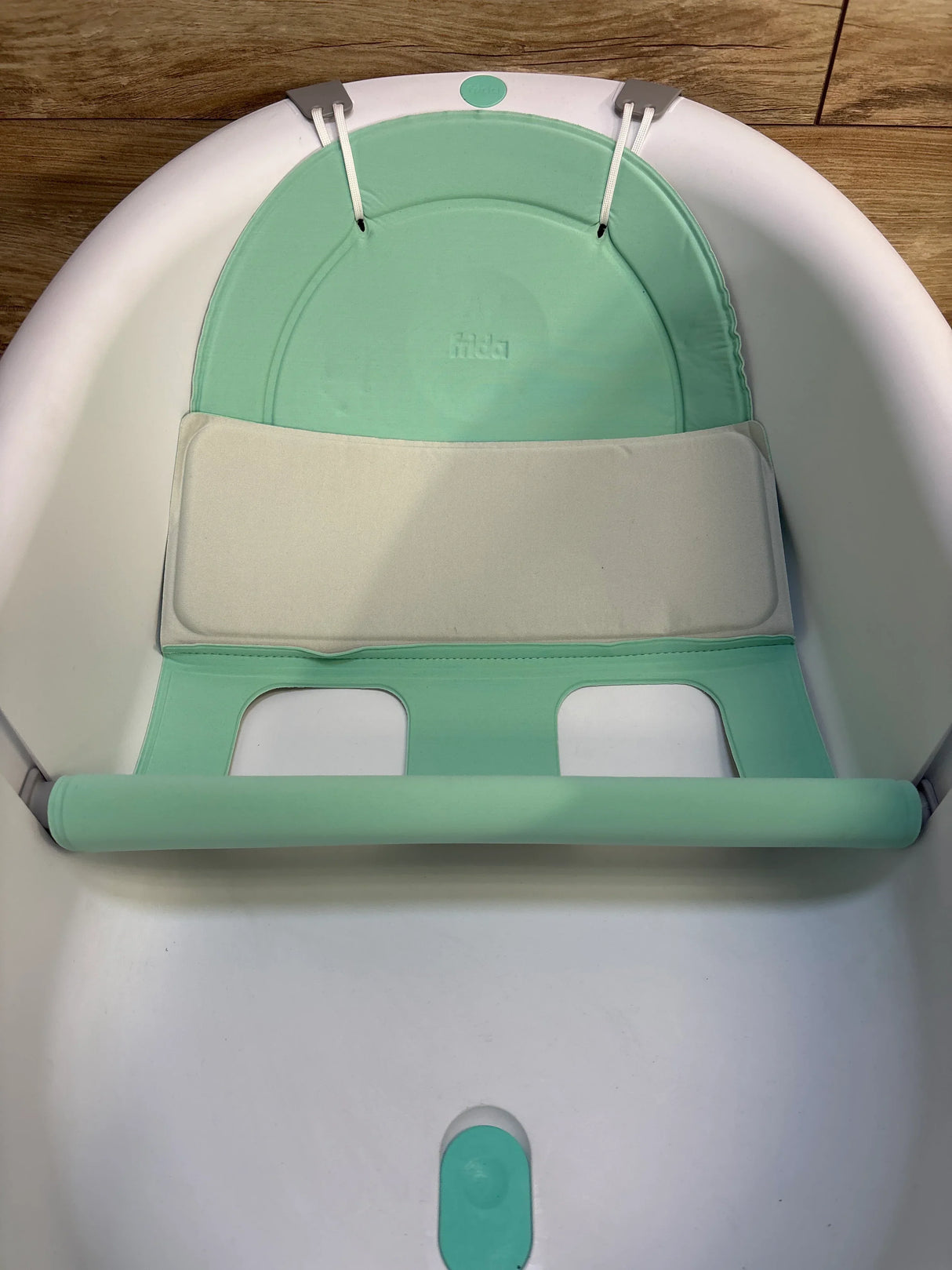Top-down view of Frida Baby 4-in-1 bath tub insert showing mint green cushioned backrest and padded seat inside white tub