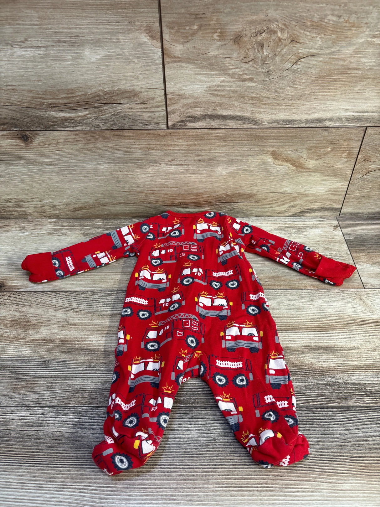 Flat lay of Wonder Nation firetruck-print infant sleeper showcasing footed legs and long sleeves with wood plank background