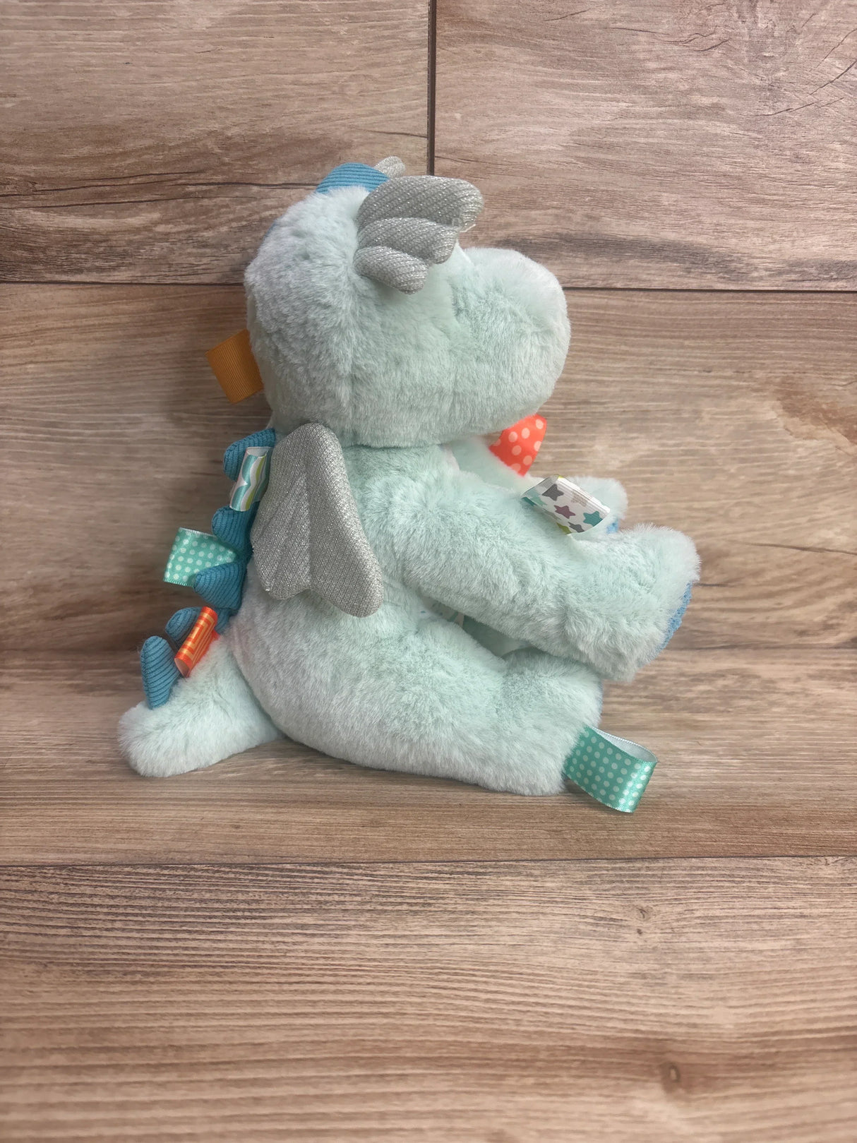 Light blue plush dragon toy with silver wings, colorful tags, on wooden background