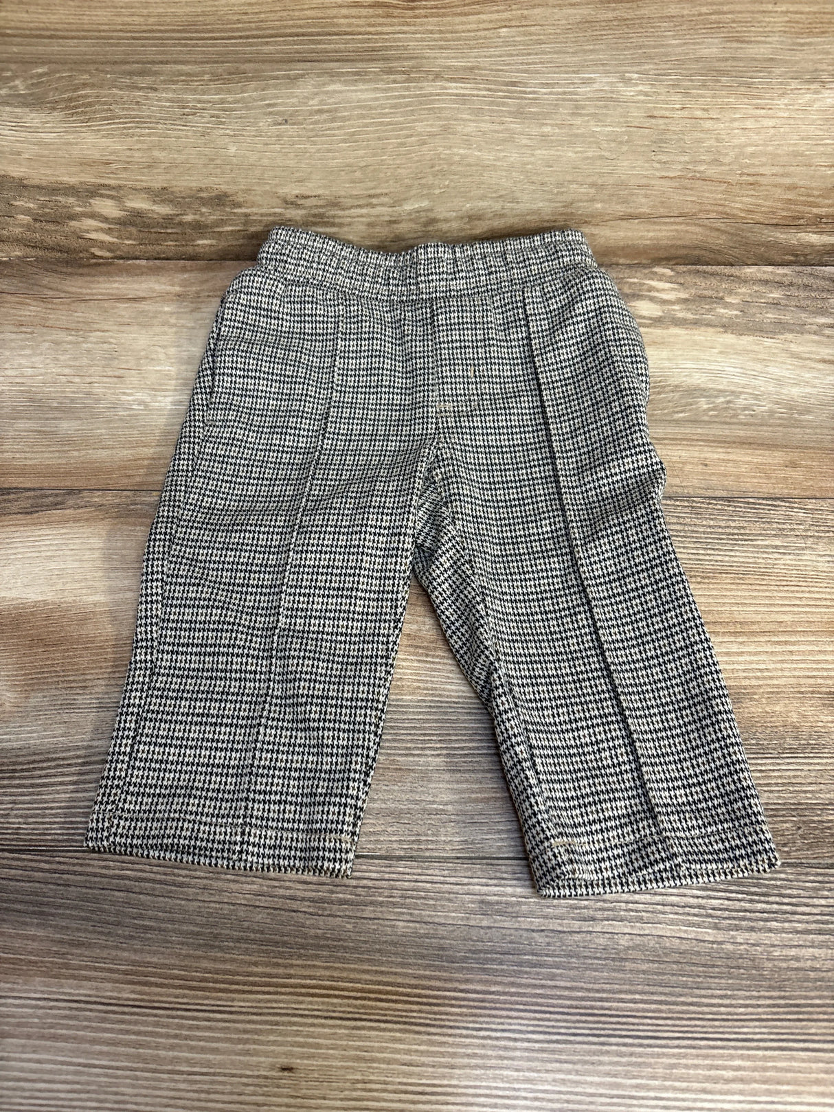 Flat lay of baby houndstooth tapered knit pants showing elastic waistband, center front creases, and tapered legs on wood background