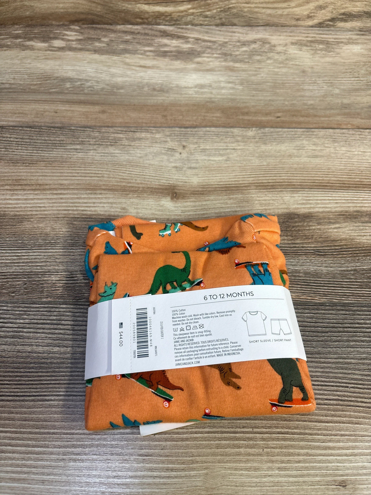 Front view of orange 2-piece baby pajama set with skateboarding dinosaur print on top and matching pants on white background
