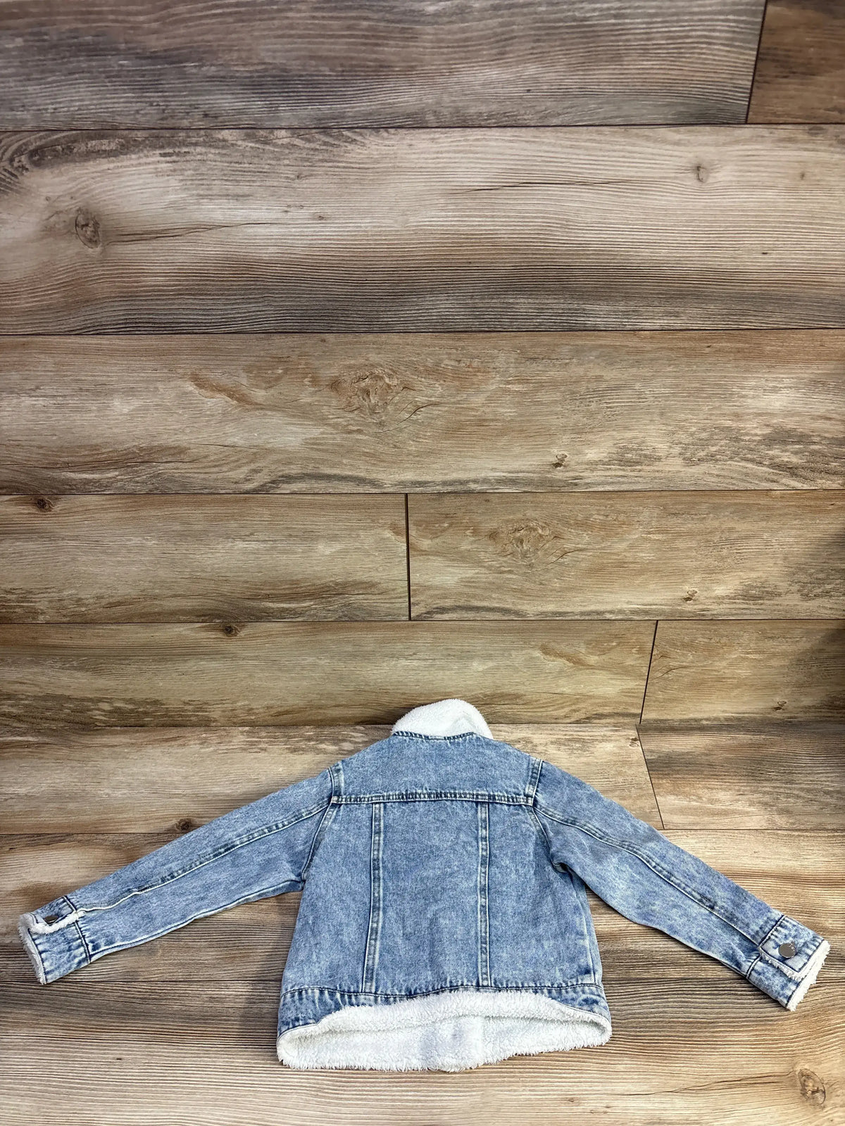 Back view of size 5T toddler light blue denim jacket showcasing sherpa collar and hem with wood plank background