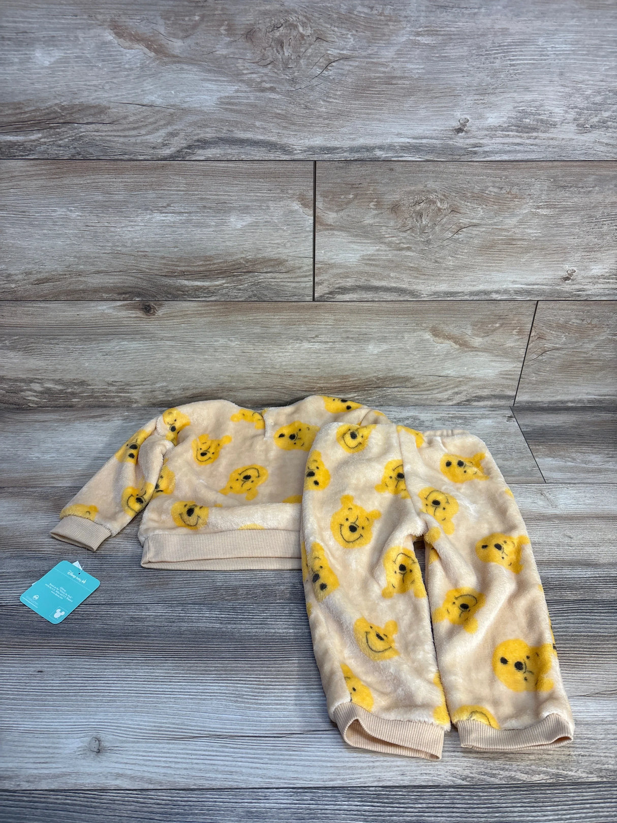 Fuzzy kids pajama set with yellow bear faces, long sleeves and pants, laid on wood floor.