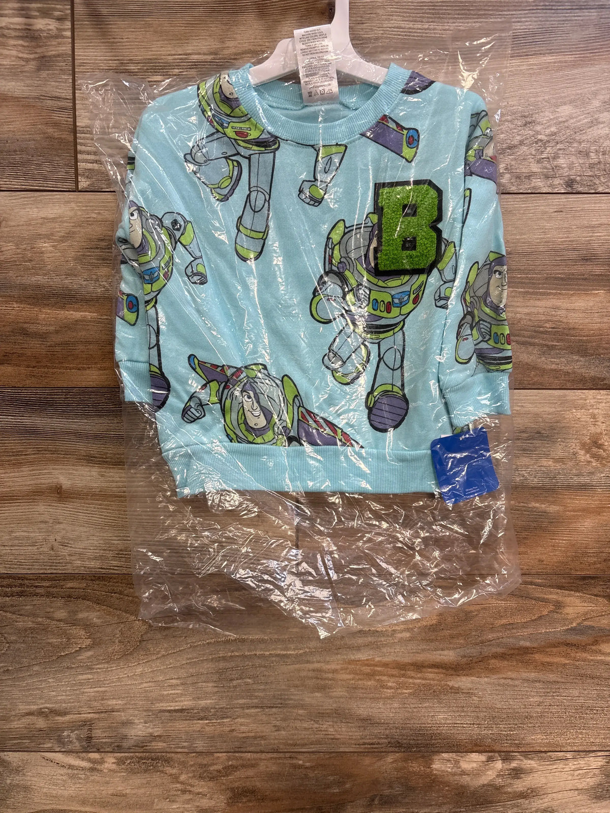Front view of blue Disney Toy Story Buzz Lightyear sweatshirt in plastic, with all-over print and green B patch