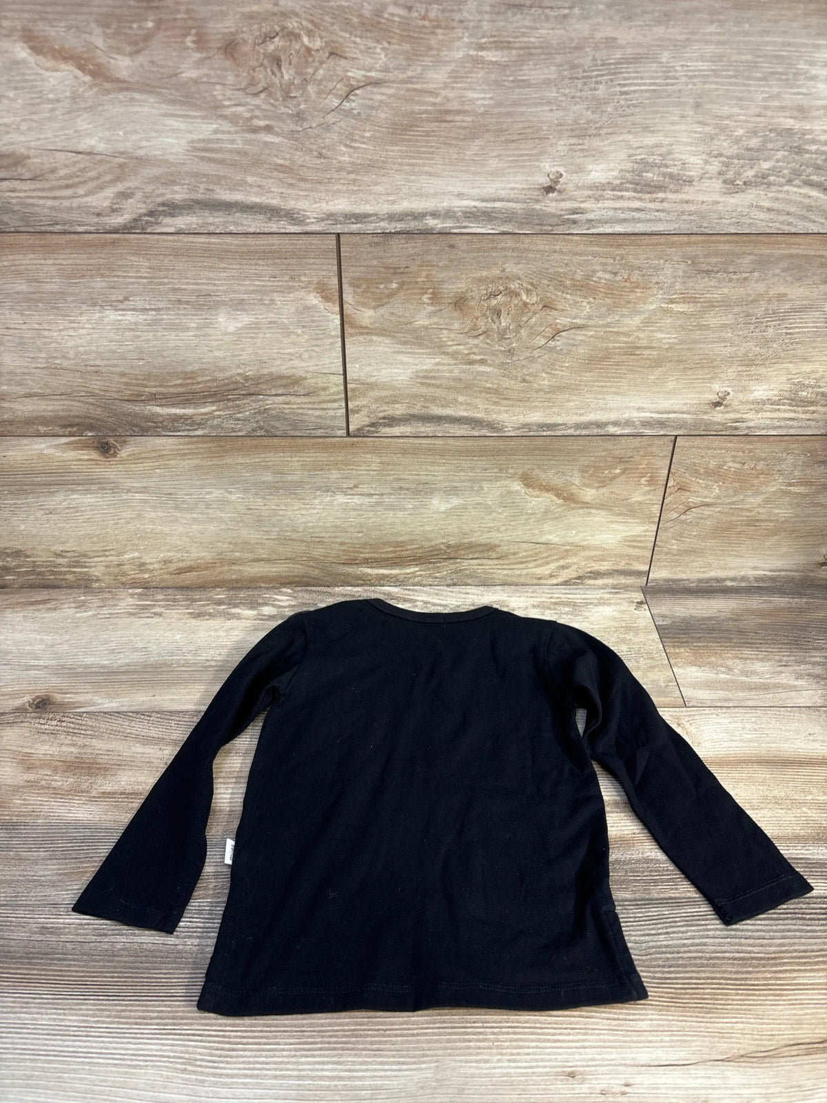 Front view of Miles Baby black basic long sleeve shirt, size 2T, with long sleeves on a wood background