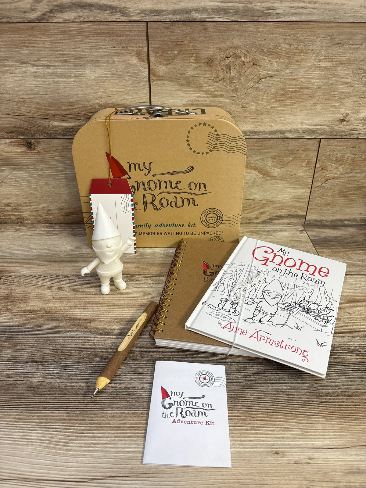 Front view of My Gnome On The Roam Adventure Kit with gnome, book, journal, wooden pen, and carrying case on a wood surface
