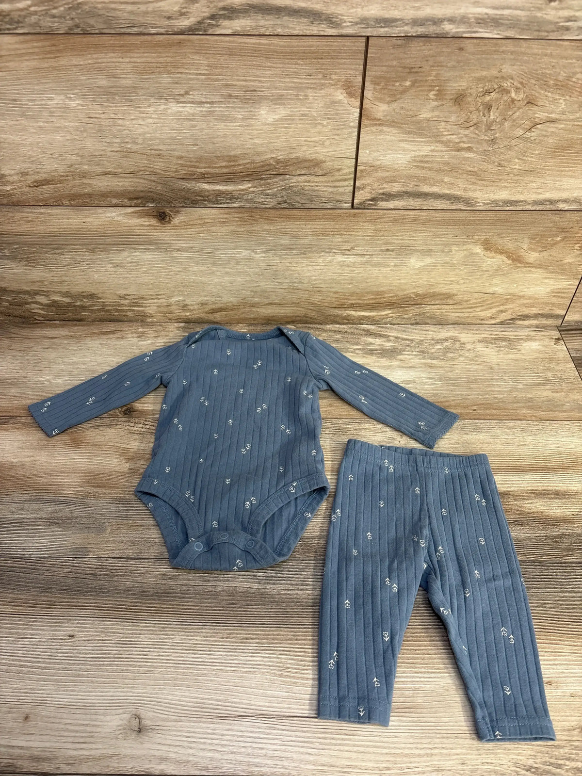 Flat lay of blue ribbed two piece baby set, long sleeve bodysuit and leggings with small white floral print on wood background