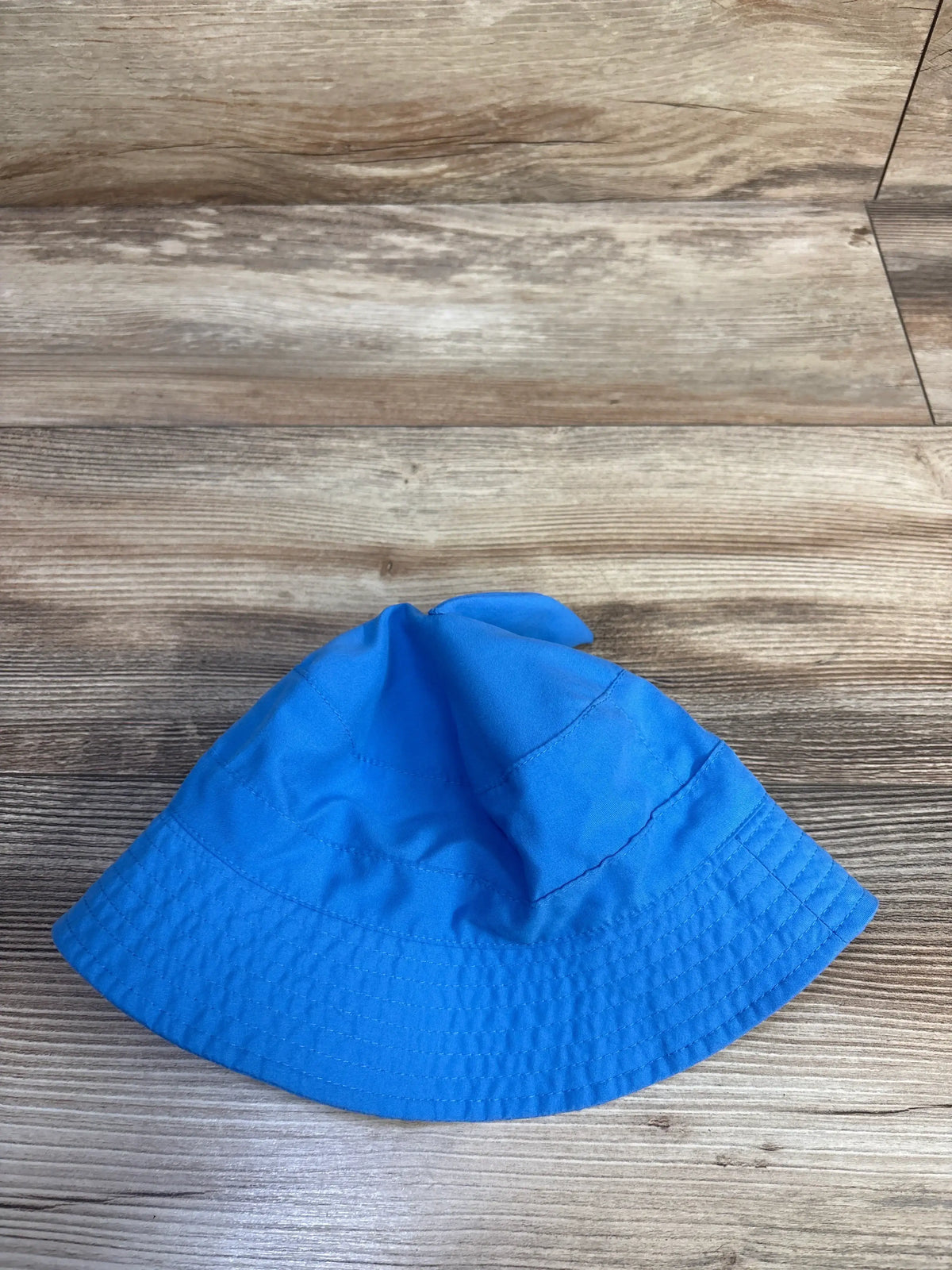 Top view of a blue Just One You shark bucket hat showcasing its shark fin design on a wood-look floor