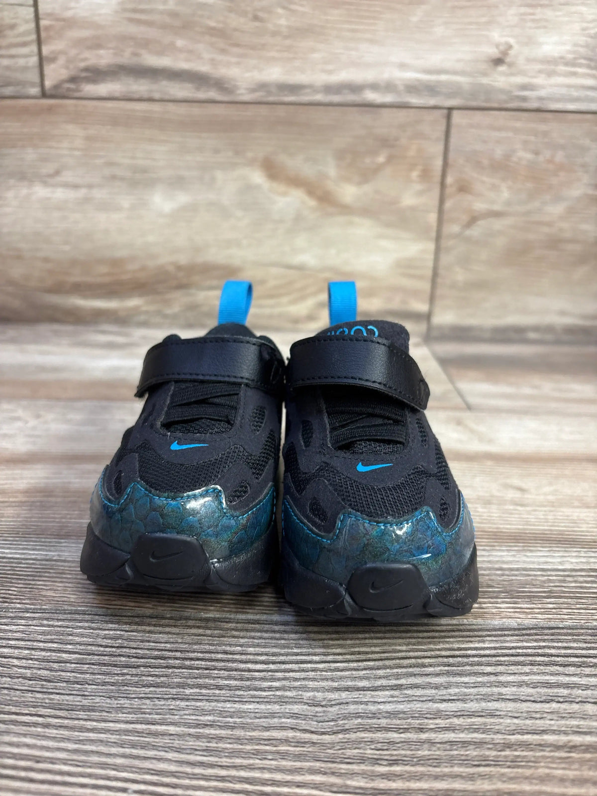 Front view of Nike Air Max 200 toddler sneakers, black mesh with blue iridescent toe, Velcro strap, on wood floor
