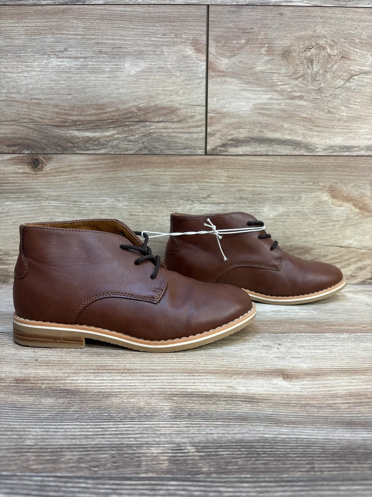 Brown leather kids dress shoes with black laces on wooden background
