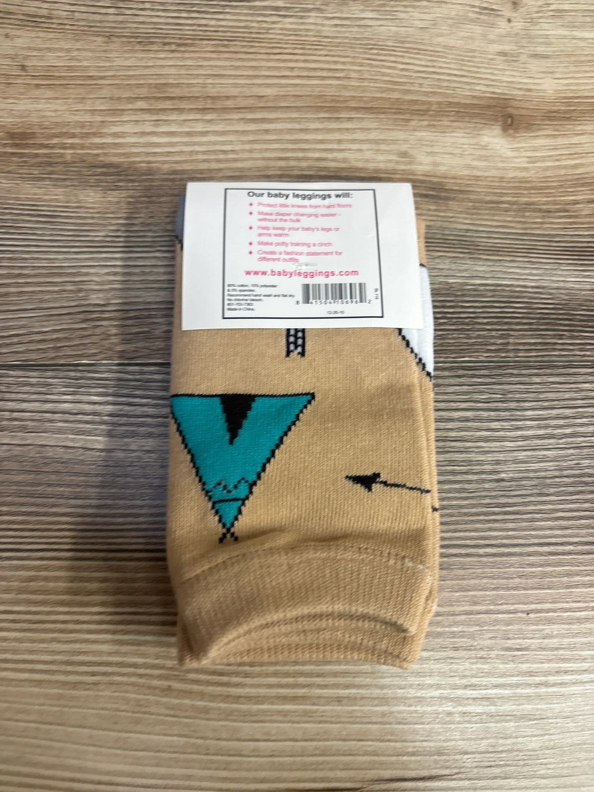 Folded tan baby leggings with geometric teal arrow print and product label on wood surface.
