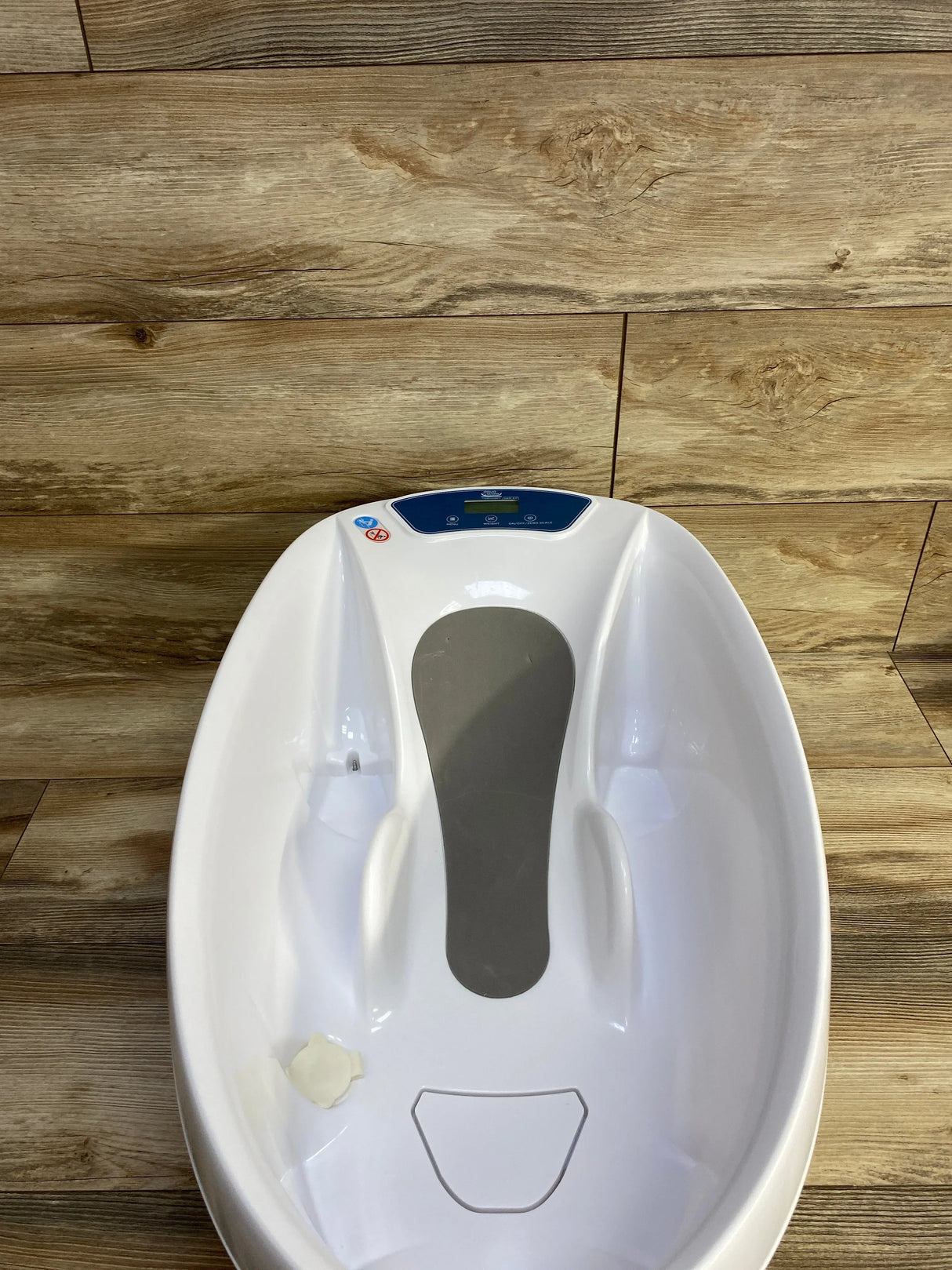Overhead view of AquaScale 3-in-1 infant tub showing digital display, gray non-slip pad, and contoured seat on wood floor