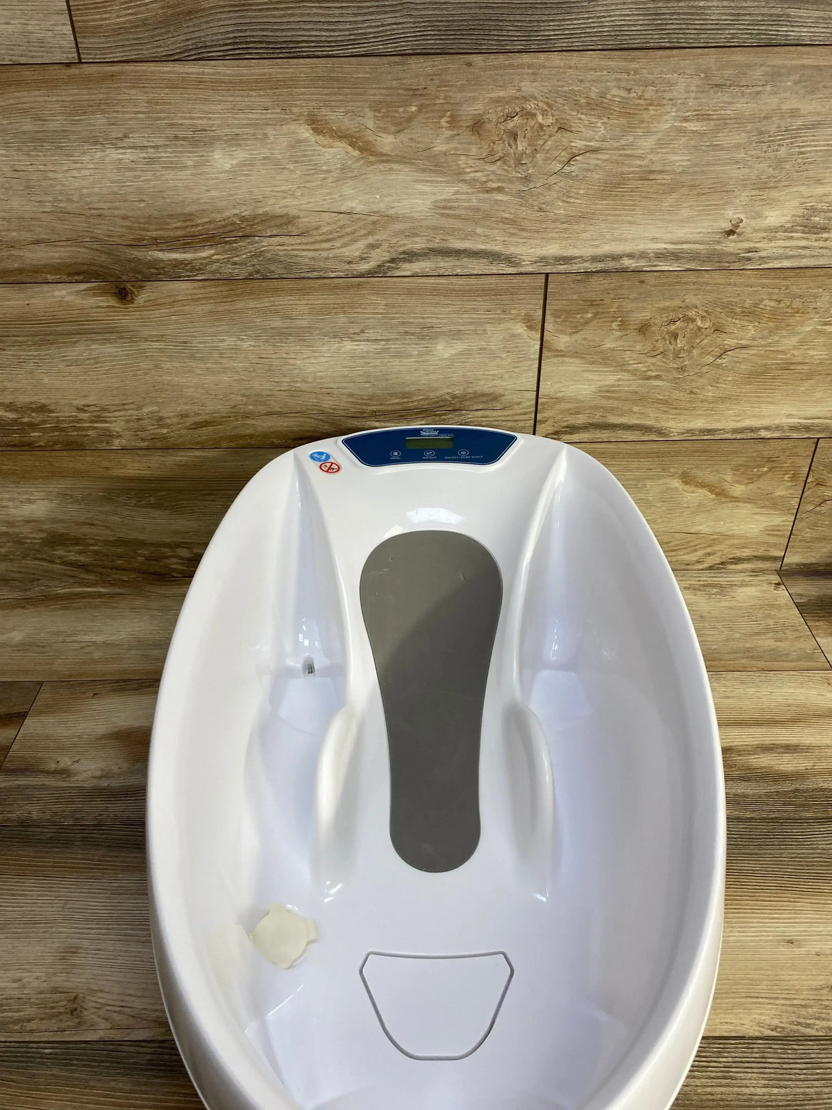 Overhead view of AquaScale 3-in-1 infant tub showing digital display, gray non-slip pad, and contoured seat on wood floor