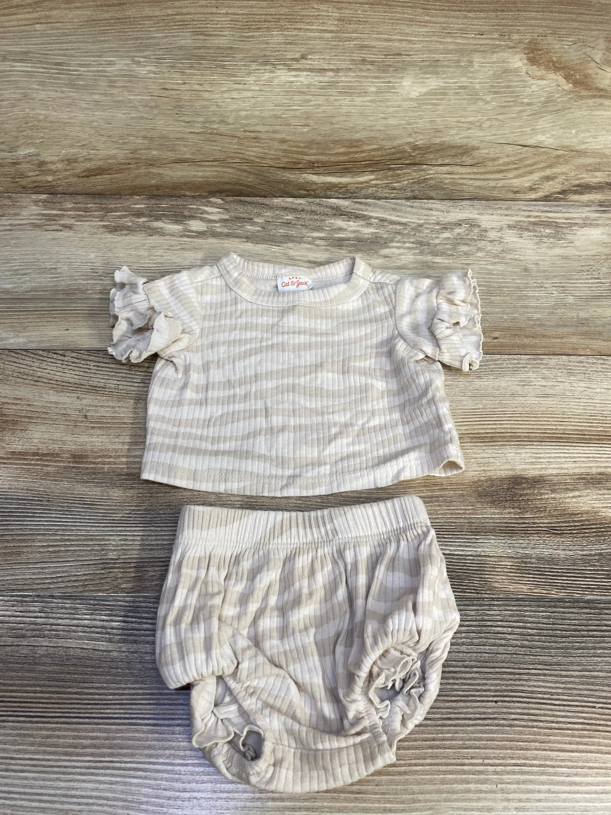 Top-down view of ivory newborn ribbed two-piece: short-sleeve ruffle shirt and bloomers showing ribbed texture on wood background