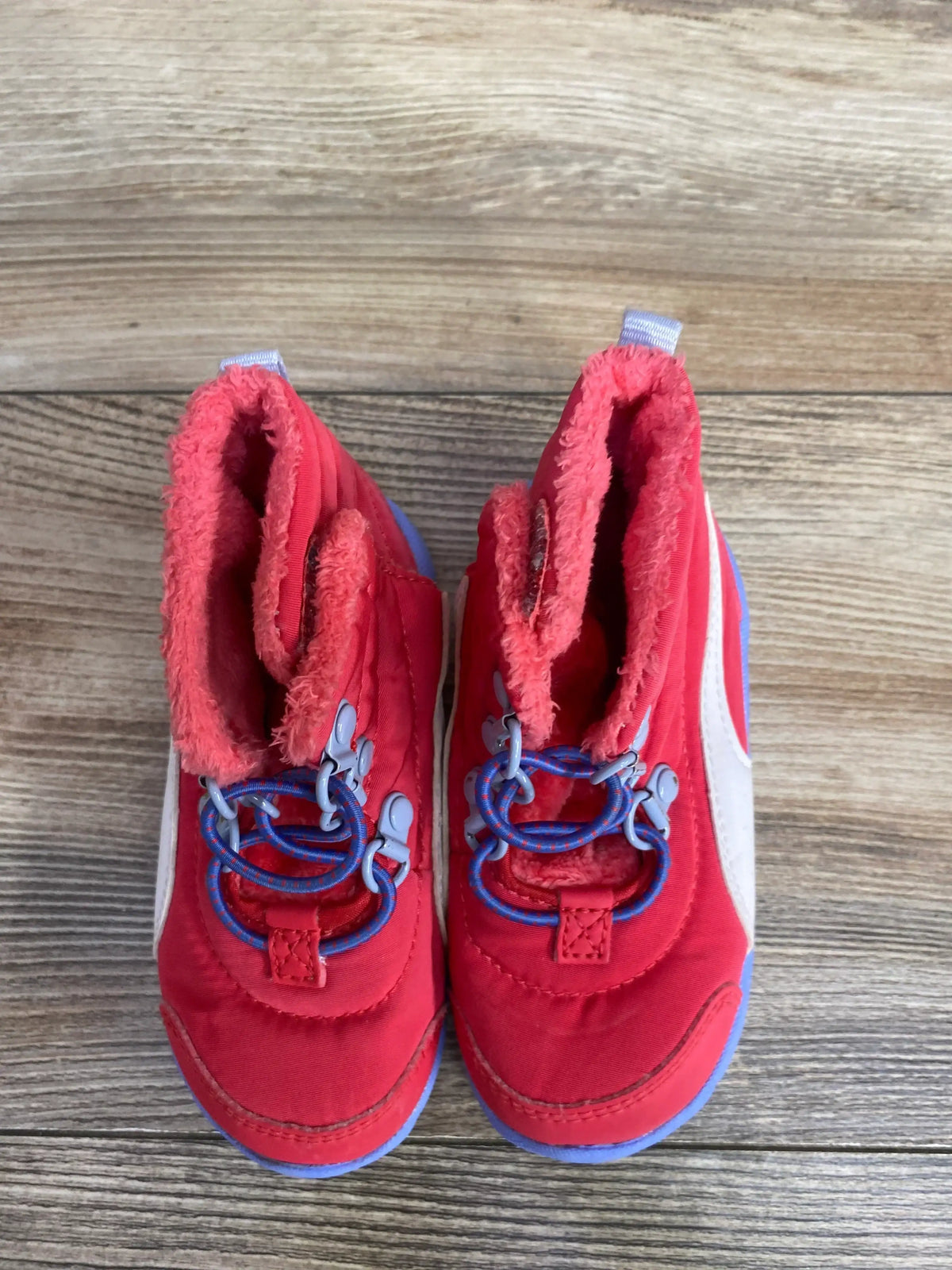 Top view of Puma Bao 3 AC snow boots size 6C showcasing pink upper, fuzzy lining, blue bungee laces and lavender soles on wooden floor
