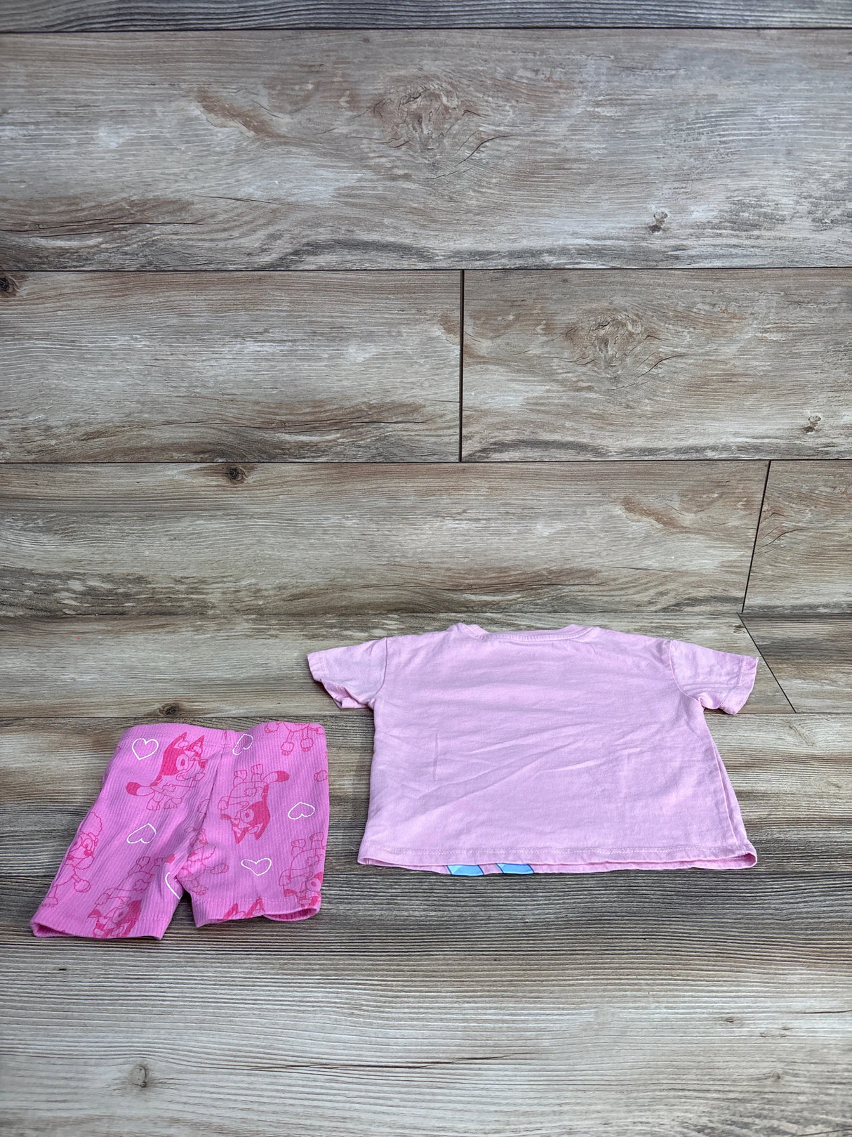 Children's pink short sleeve t-shirt and pink shorts with cartoon characters on wood floor