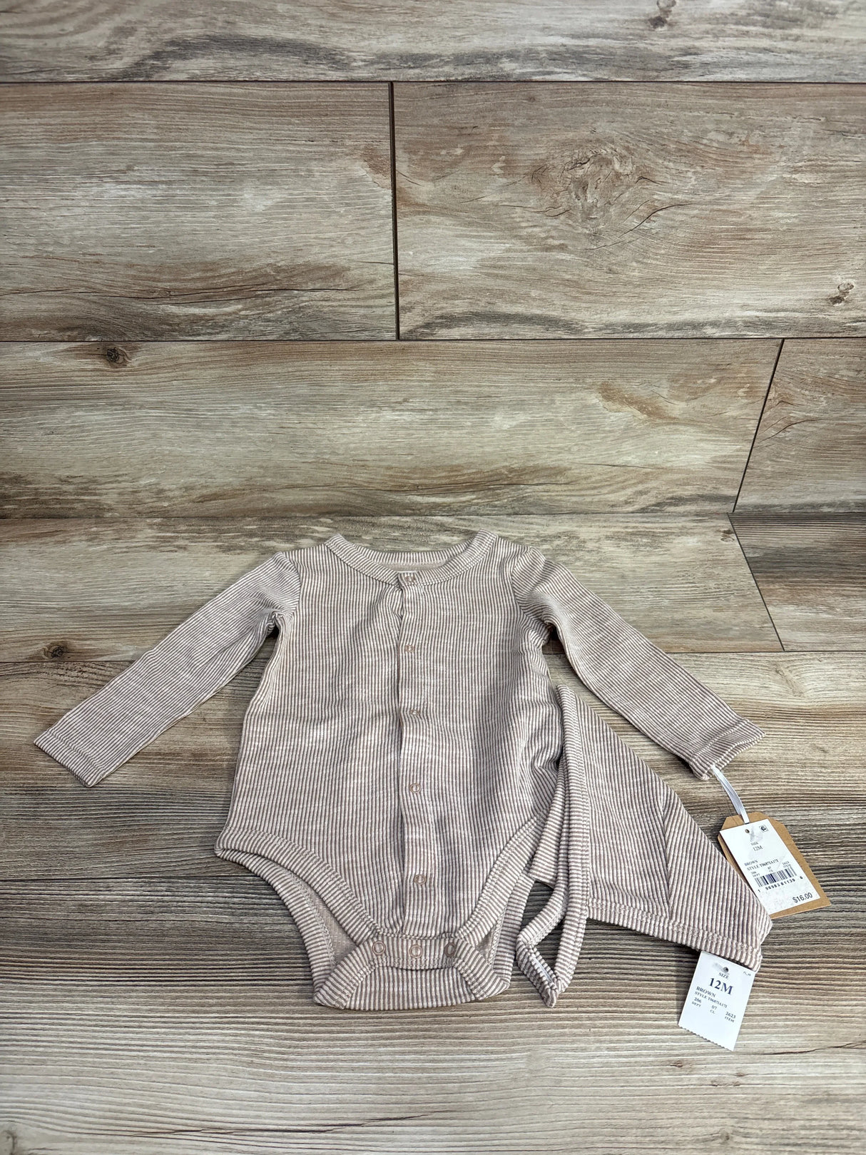 Striped beige long sleeve baby bodysuit with tags, size 12M, on wood background