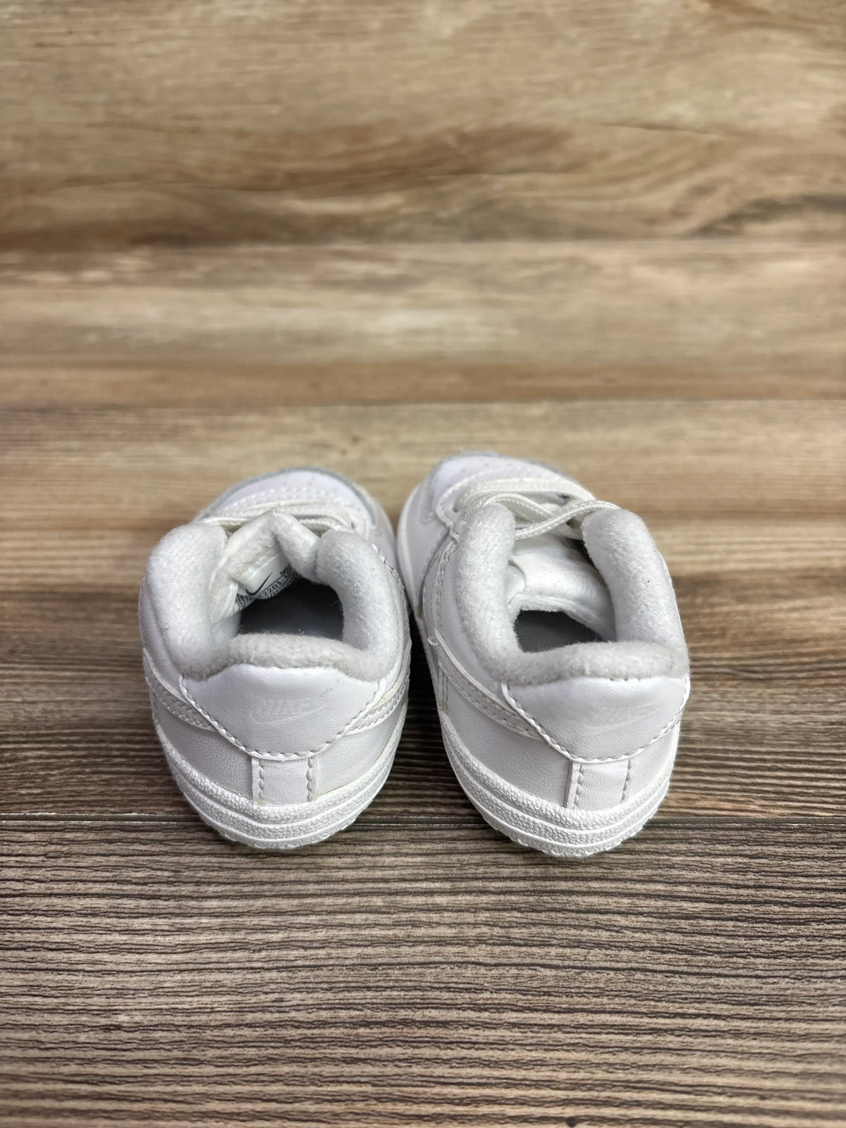 Rear view of Nike Air Force 1 CB Triple White sneakers showcasing padded collars and textured soles on a wood surface