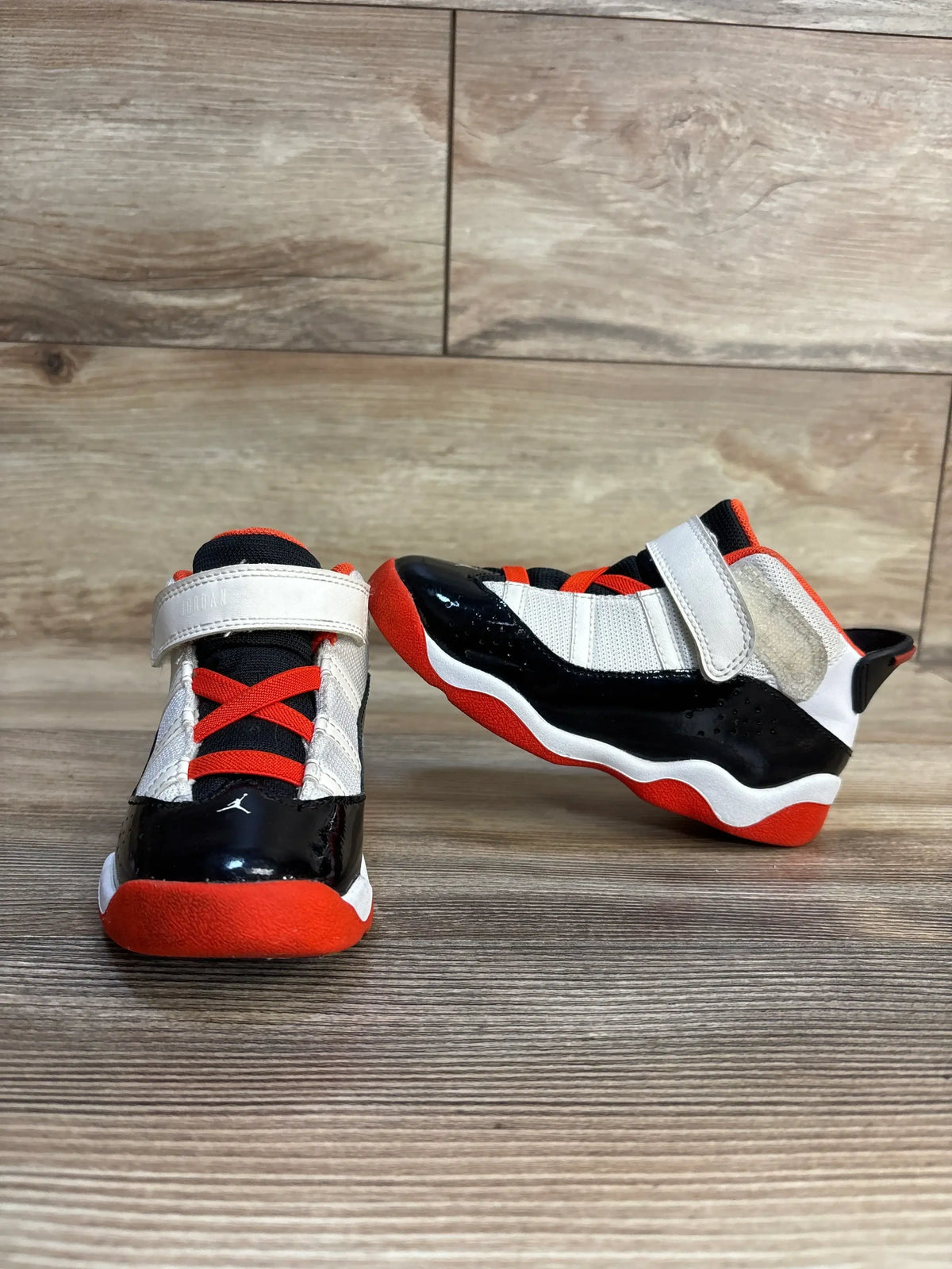 Front and side view of Air Jordan 6 Rings TD sneakers, white mesh, black patent mudguard, orange accents, Velcro strap